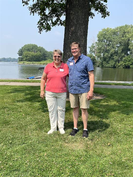 A man and woman standing in grass next to a tree