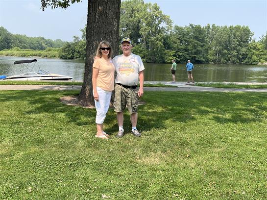 A man and woman standing in grass next to a tree