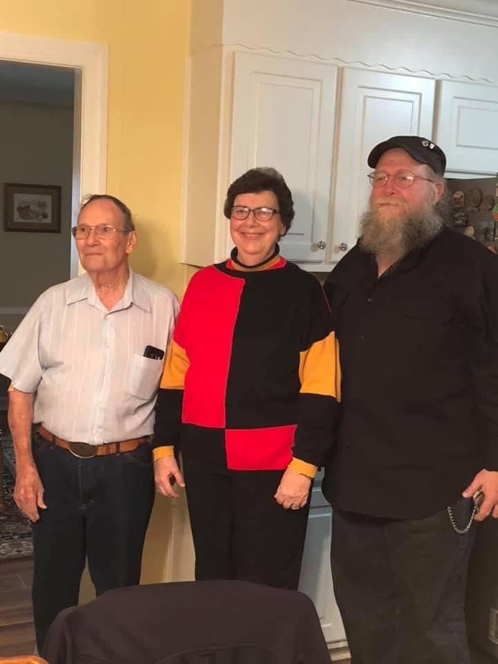 Three friends stand together smiling in a comfortable living room, sharing a joyful moment.