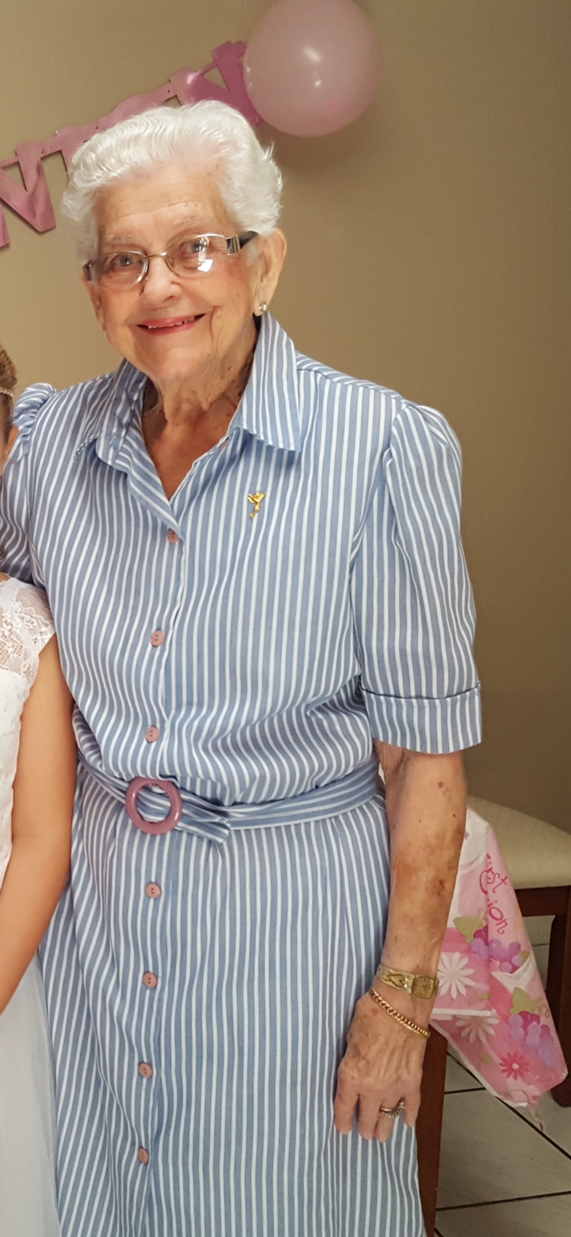 Elderly woman in striped dress embraces young girl in white dress, sharing a joyful moment indoors.