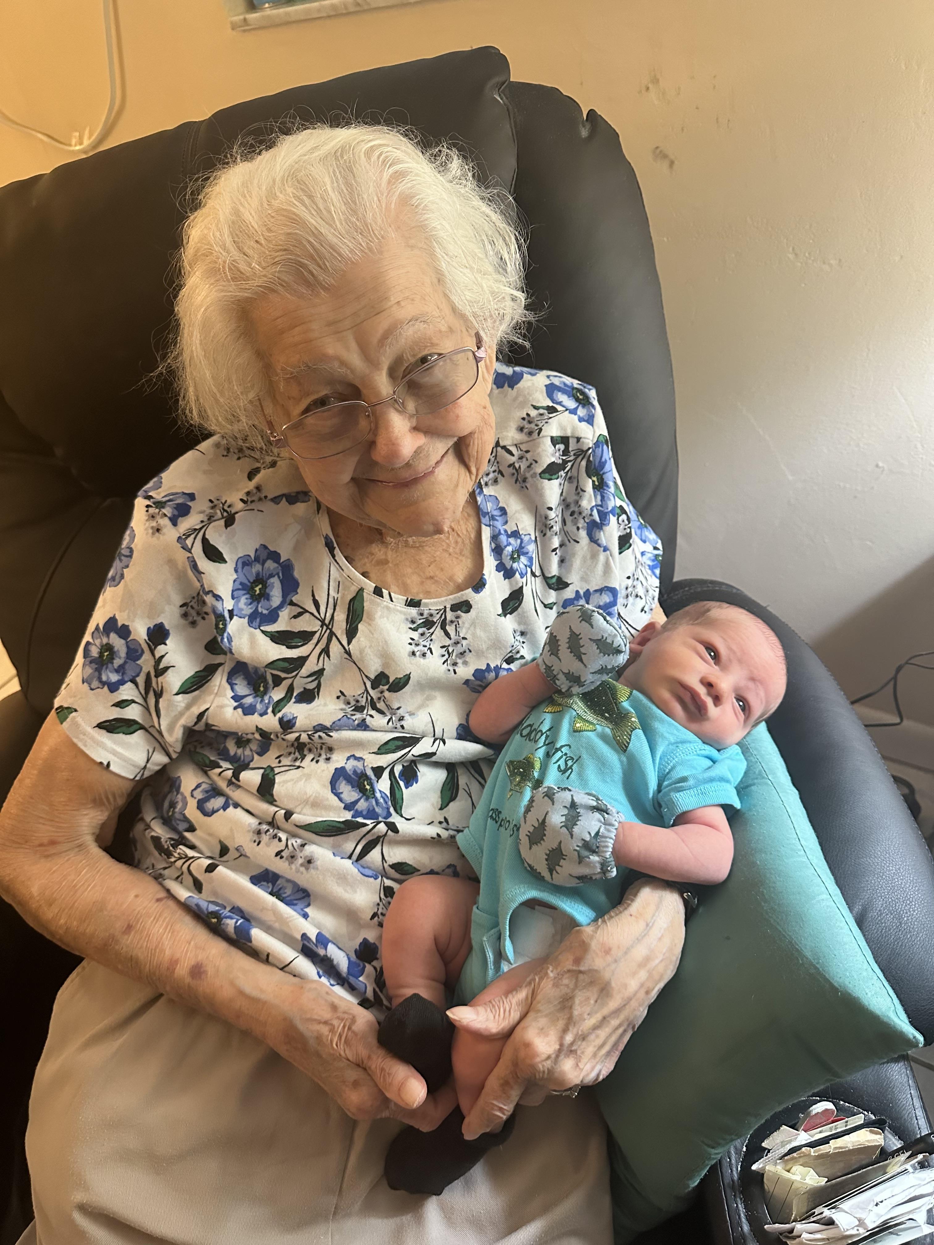 Grandmother smiles while holding her newborn grandchild in a comfortable chair at home.