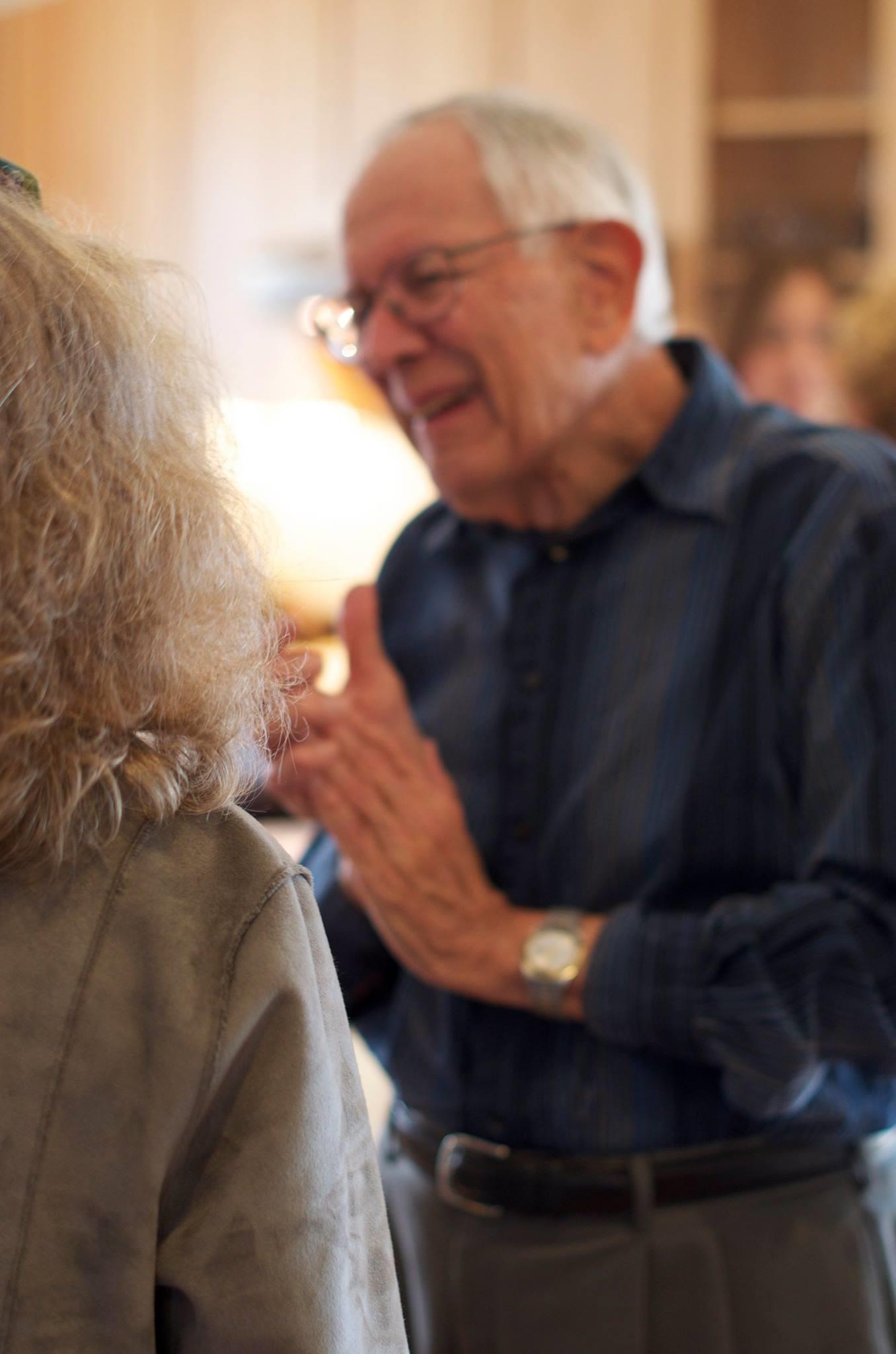 An elderly man gesturing warmly during a lively conversation at a social event.