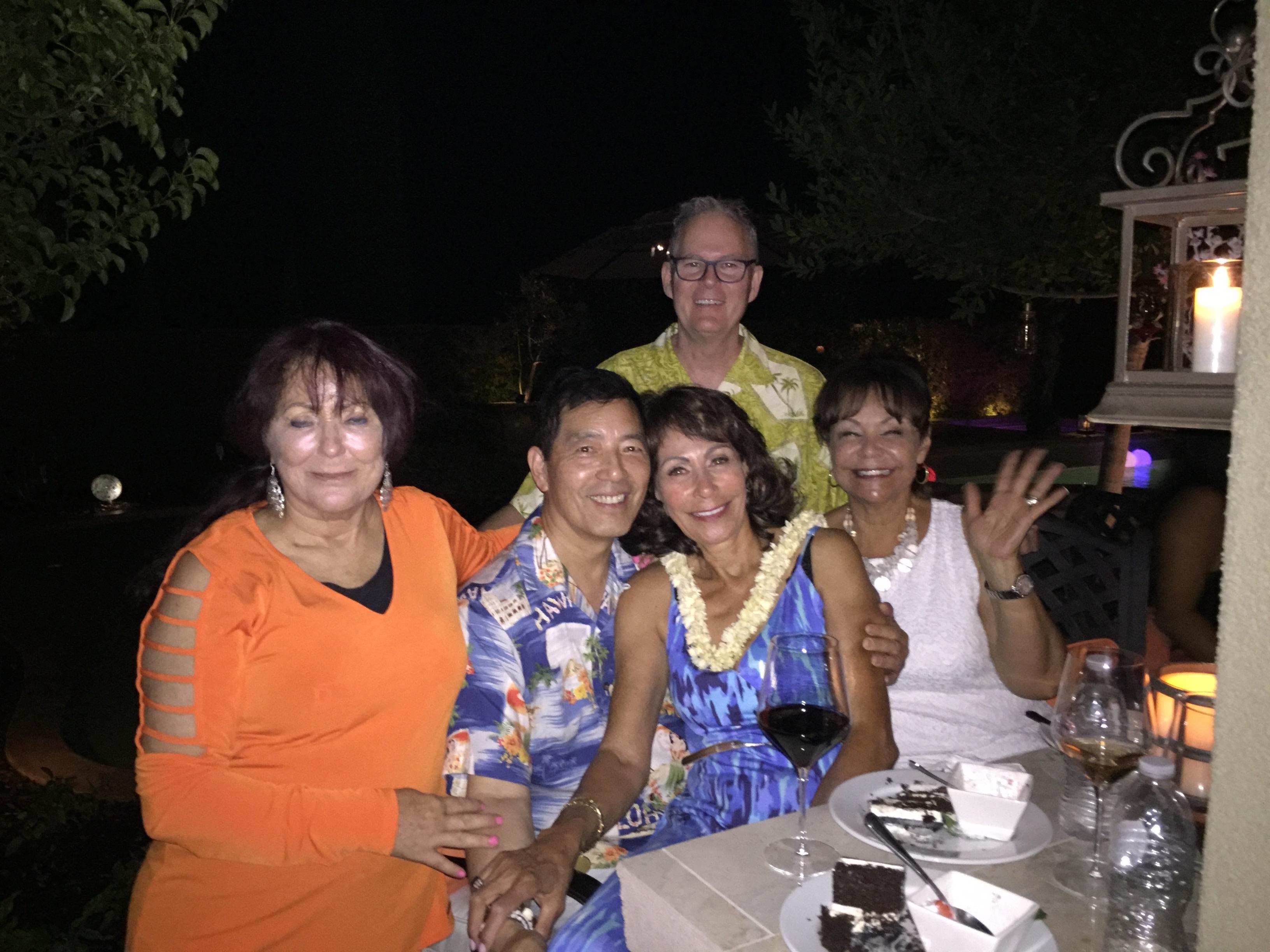 Five friends gather around a table, sharing laughs and drinks at a festive outdoor dinner.