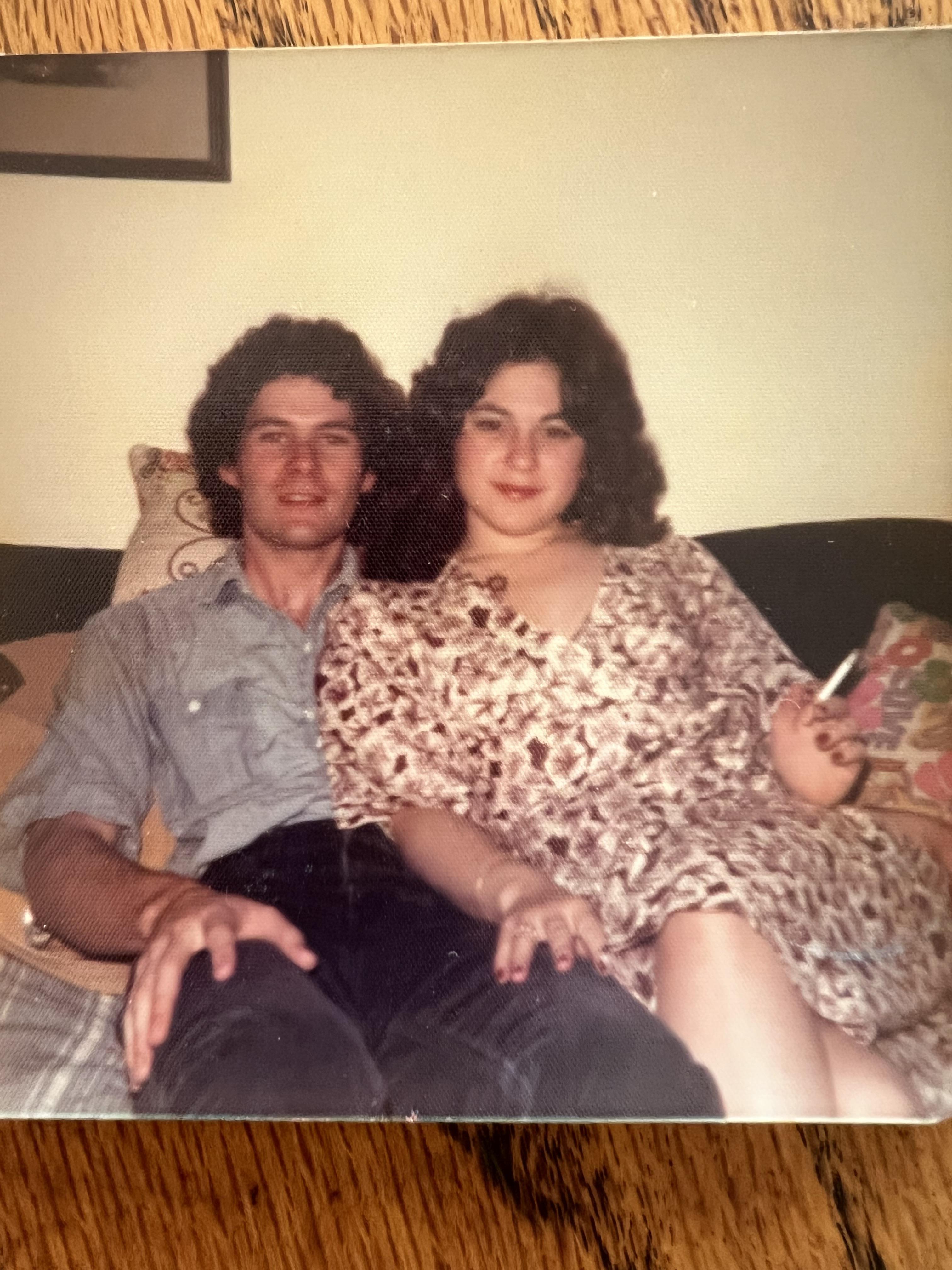 A couple relaxes together on a couch in a cozy, casual living room.