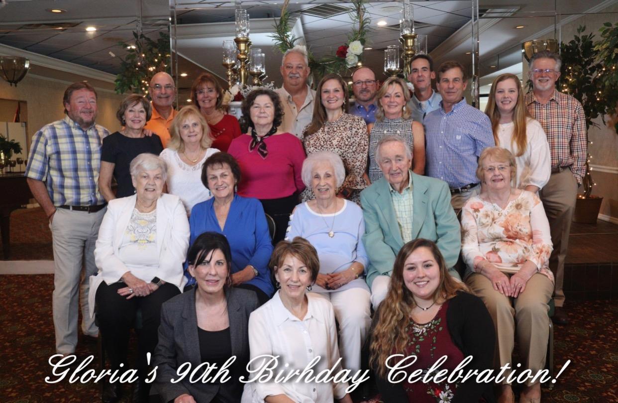 A large group gathers to celebrate a special 90th birthday with smiles and joy in a festive setting.