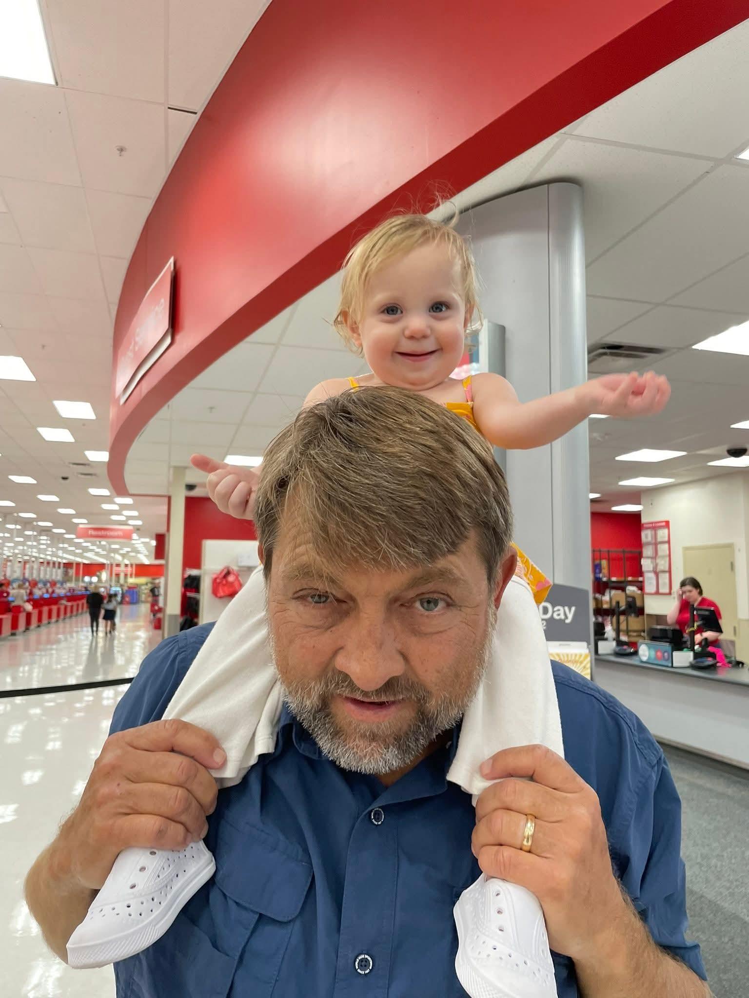 Child enjoys riding on her father's shoulders while shopping in a bright store.