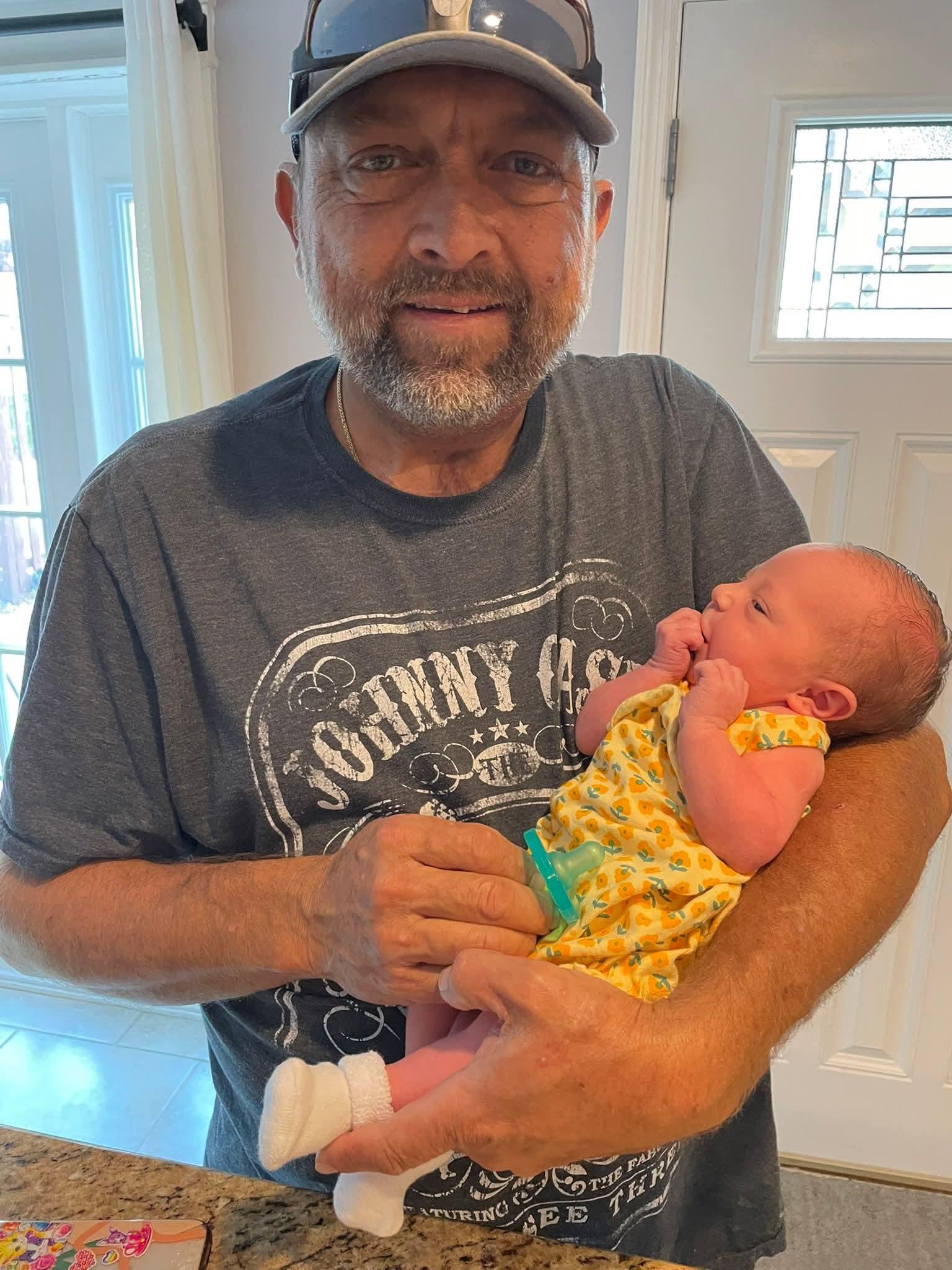 A joyful elder cradles a small baby in bright clothing, enjoying a warm moment together at home.