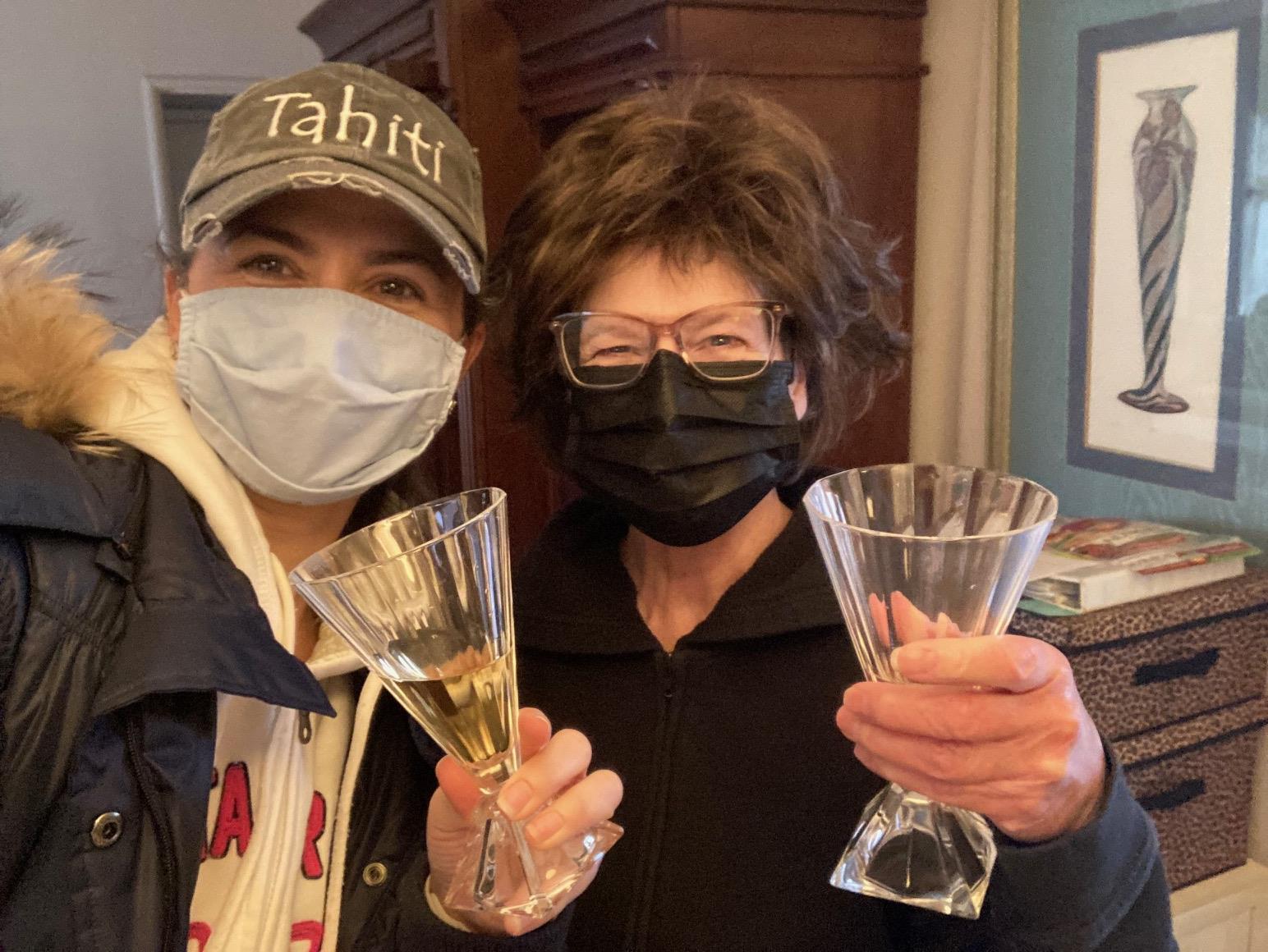 Two women wearing face masks holding glasses
