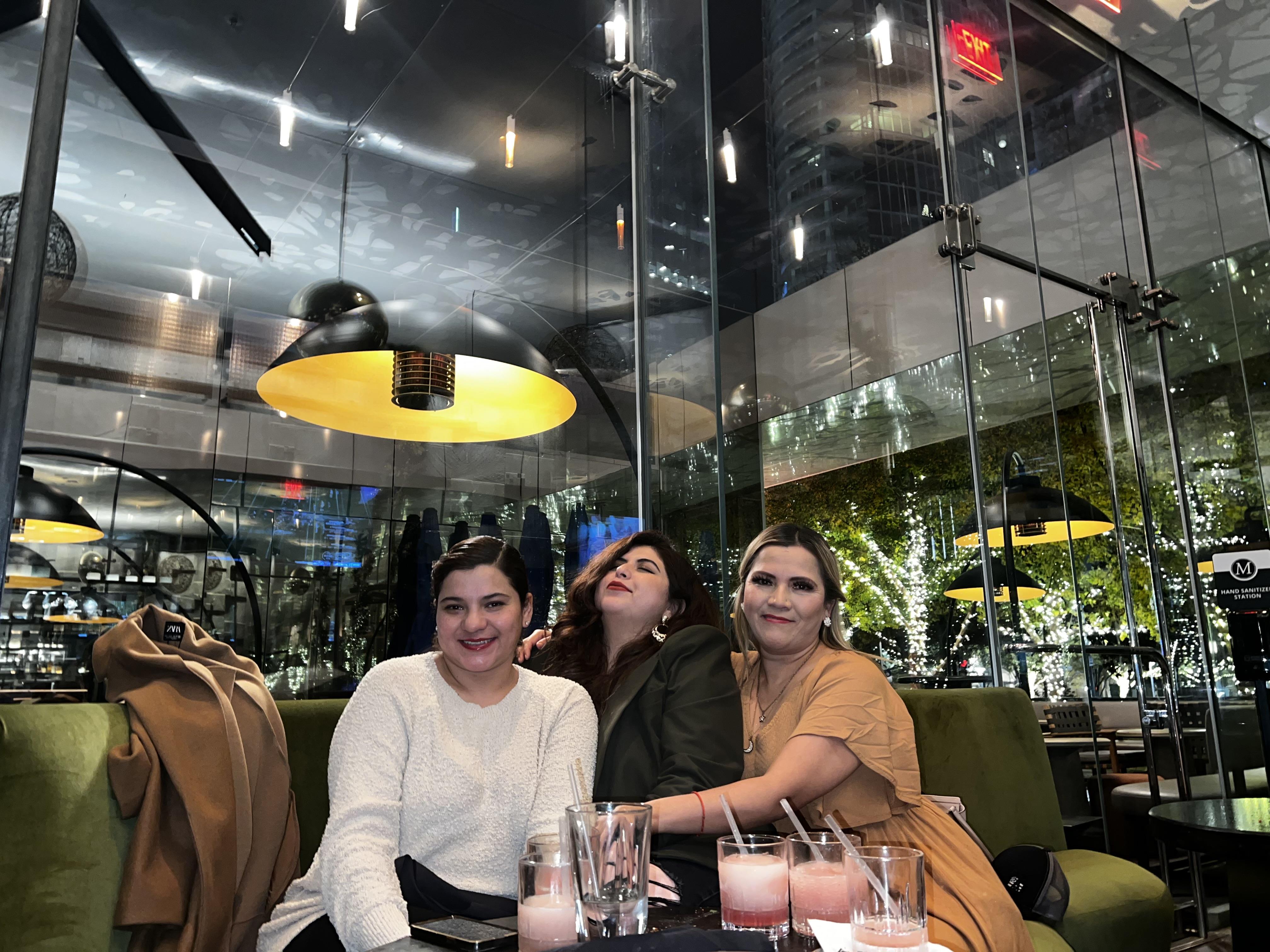 Three women relax together at a stylish cafe, sharing drinks and laughter in the evening.