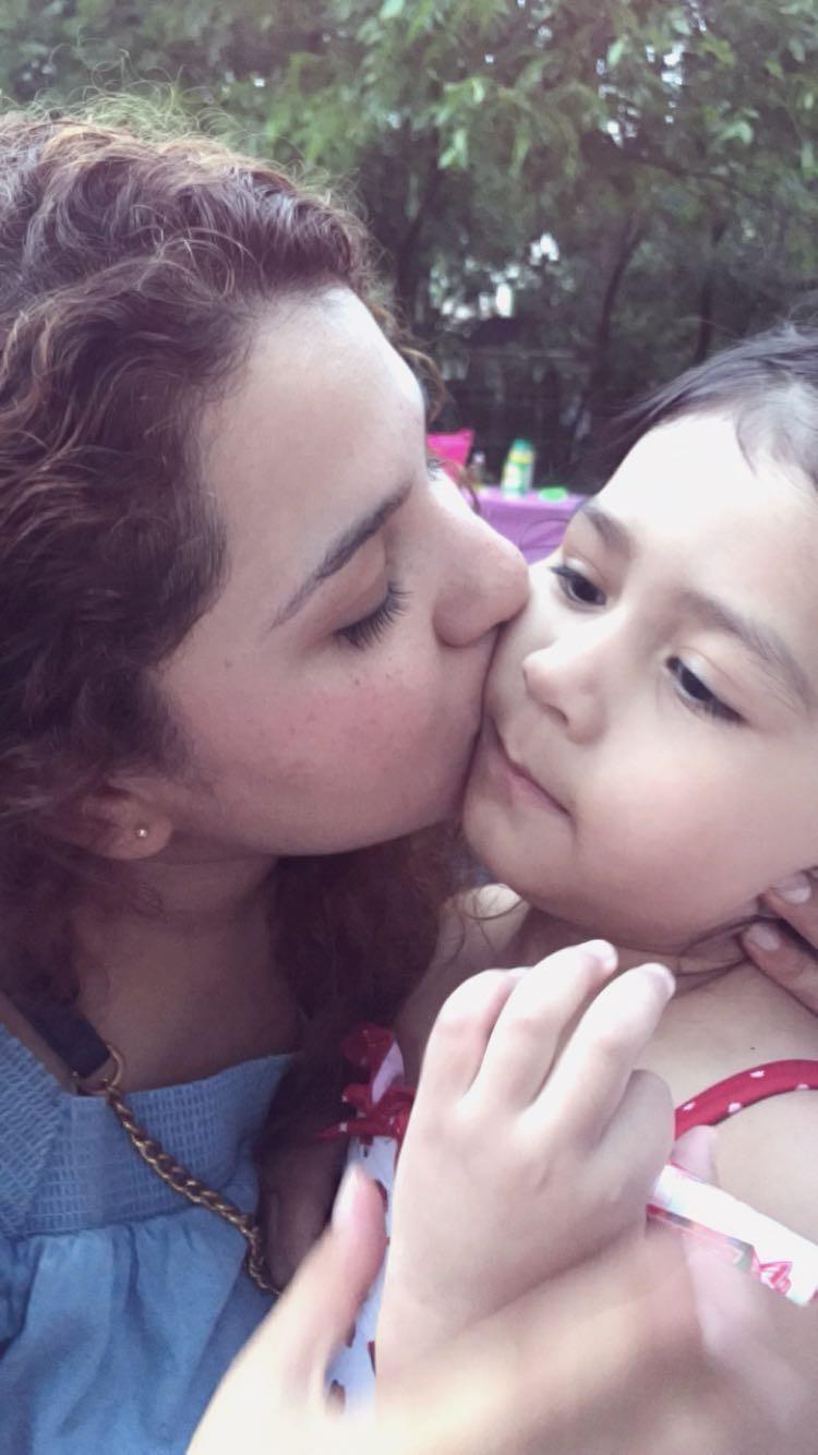 A mother kisses her daughter on the cheek while they enjoy time together in the park.