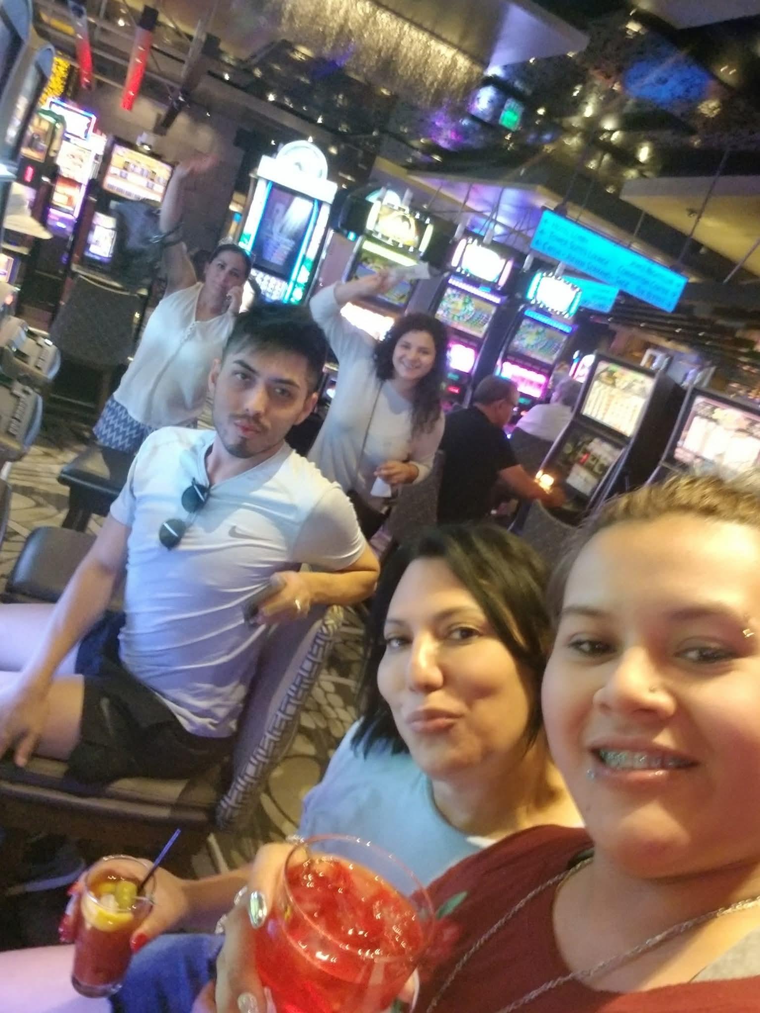 Friends gather for selfies and fun at a busy casino, filled with bright lights and slot machines.