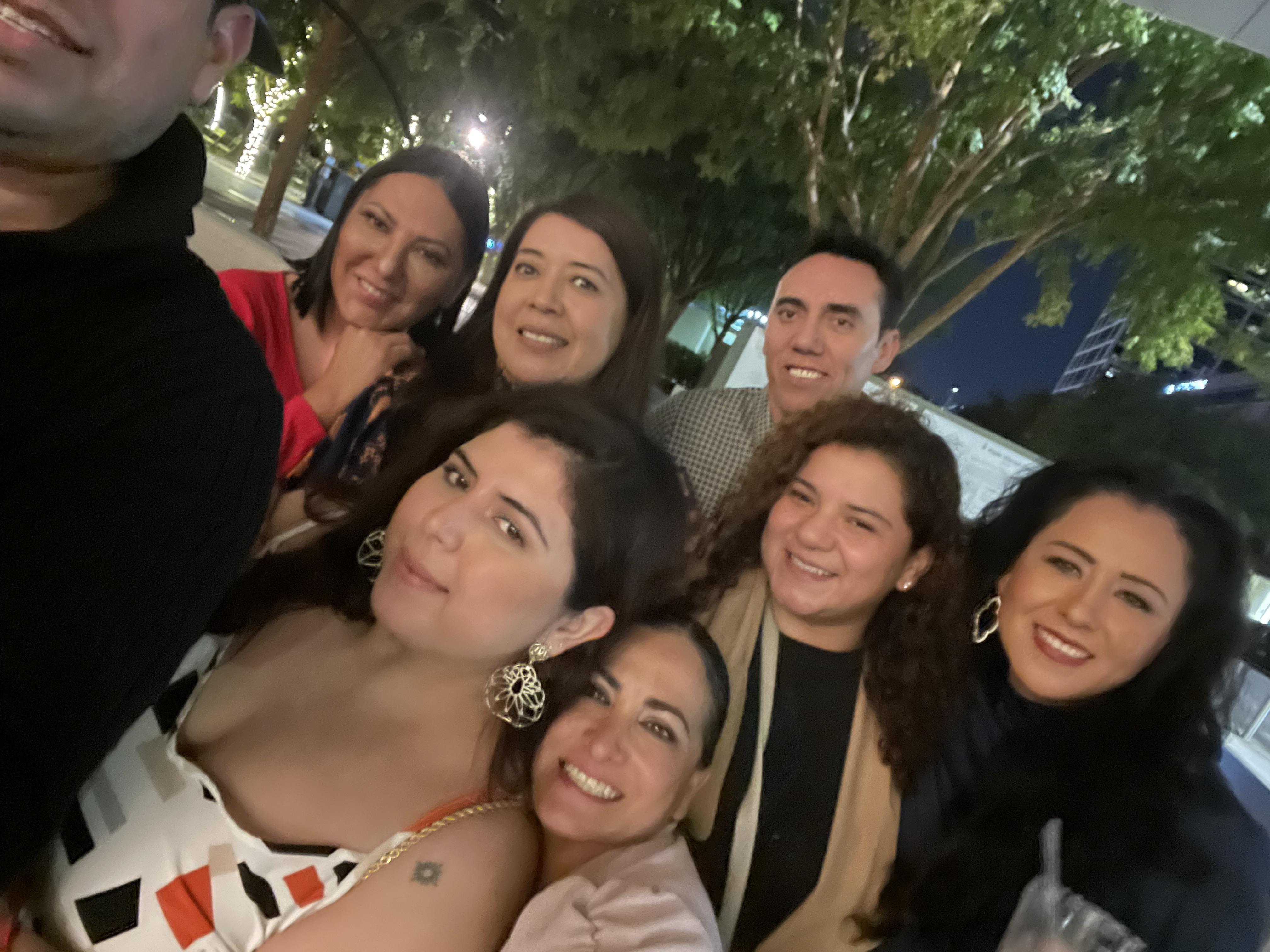 Eight friends gather and smile together in a lively city park under the stars on a summer night.