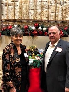A couple smiles together at a festive holiday gathering with decorations and gifts.