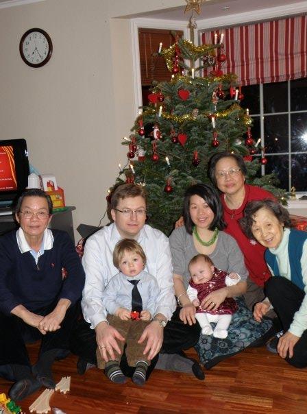 People sit together with children near a Christmas tree in a warm living room setting.