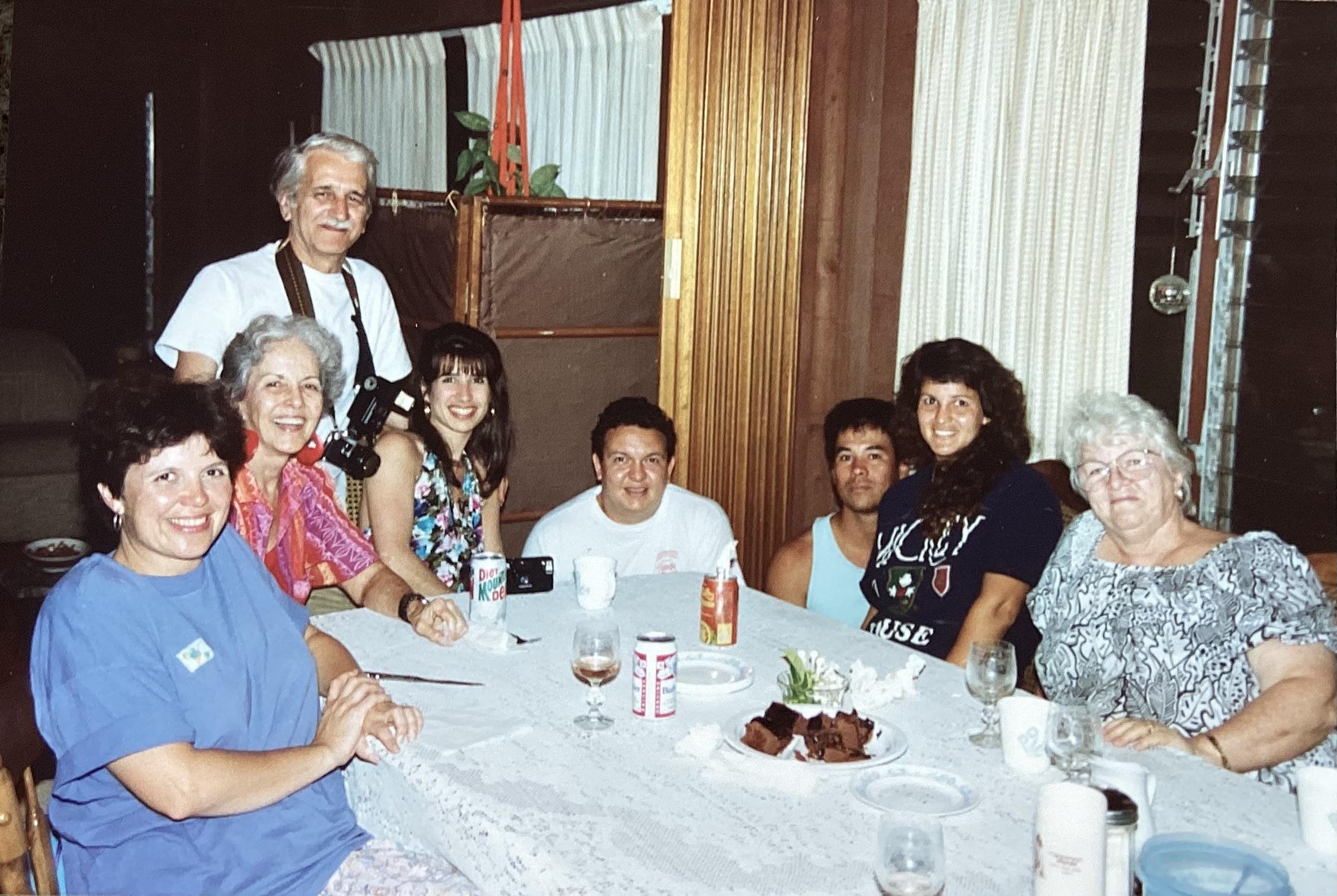 A group of people enjoy a meal together at a table with food and drinks in a home.