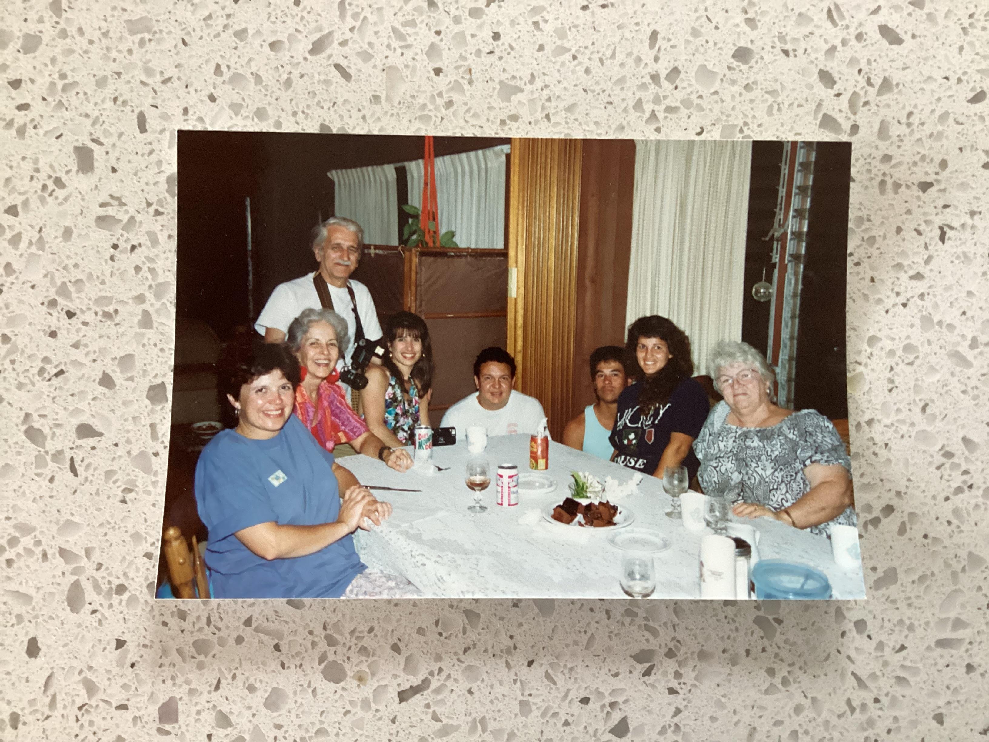 A group of eight people sit together at a table enjoying food and drinks in a casual setting.