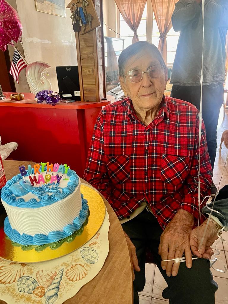 An old woman sitting at a table with a birthday cake