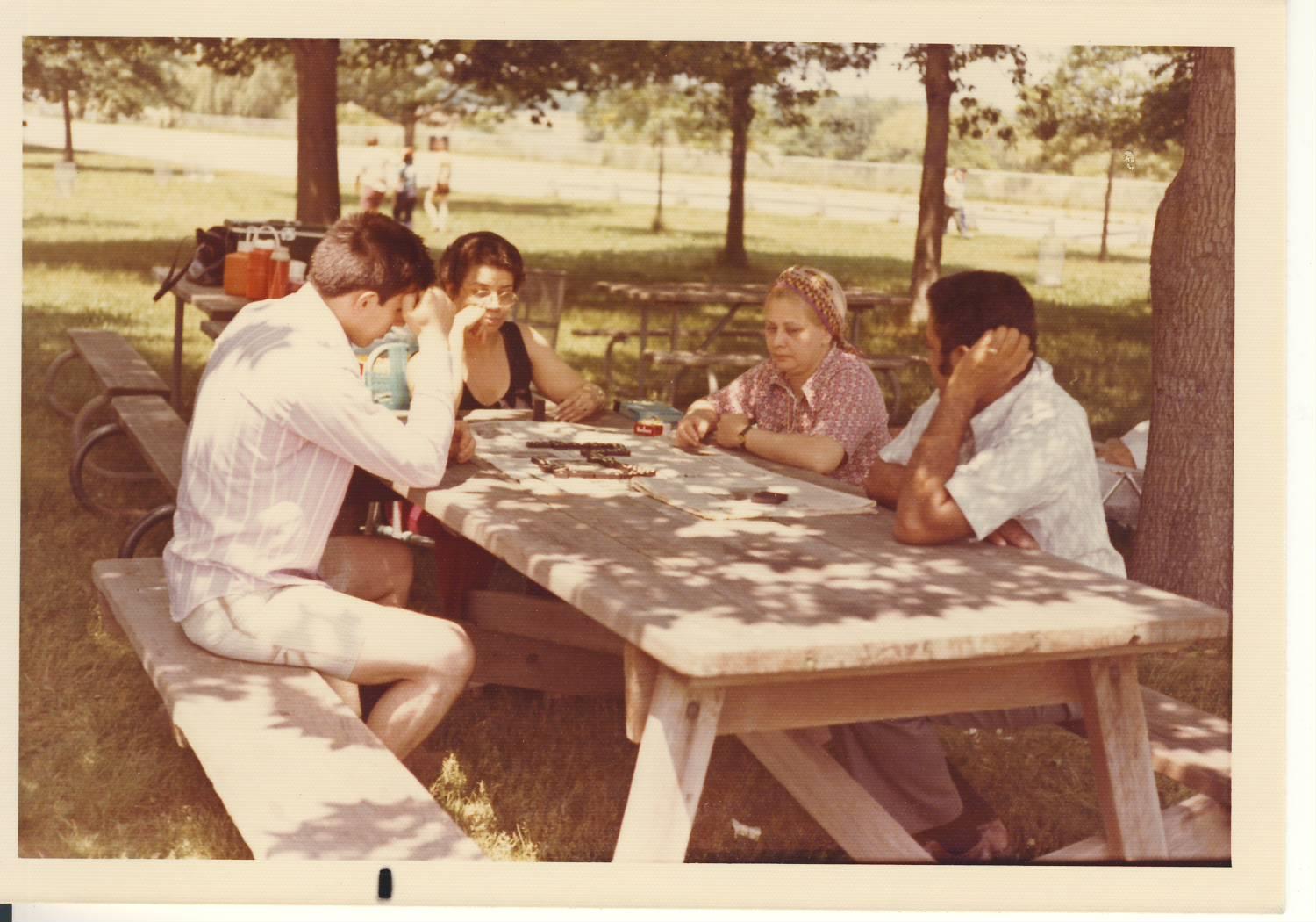 Four friends gather around a picnic table, playing games and enjoying a sunny day outdoors.