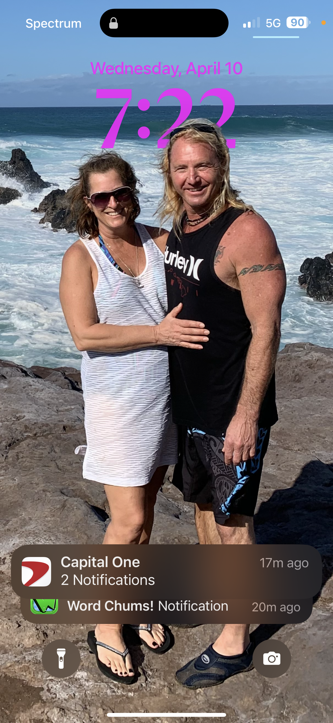 A couple stands close together on the rocks with waves crashing behind them.