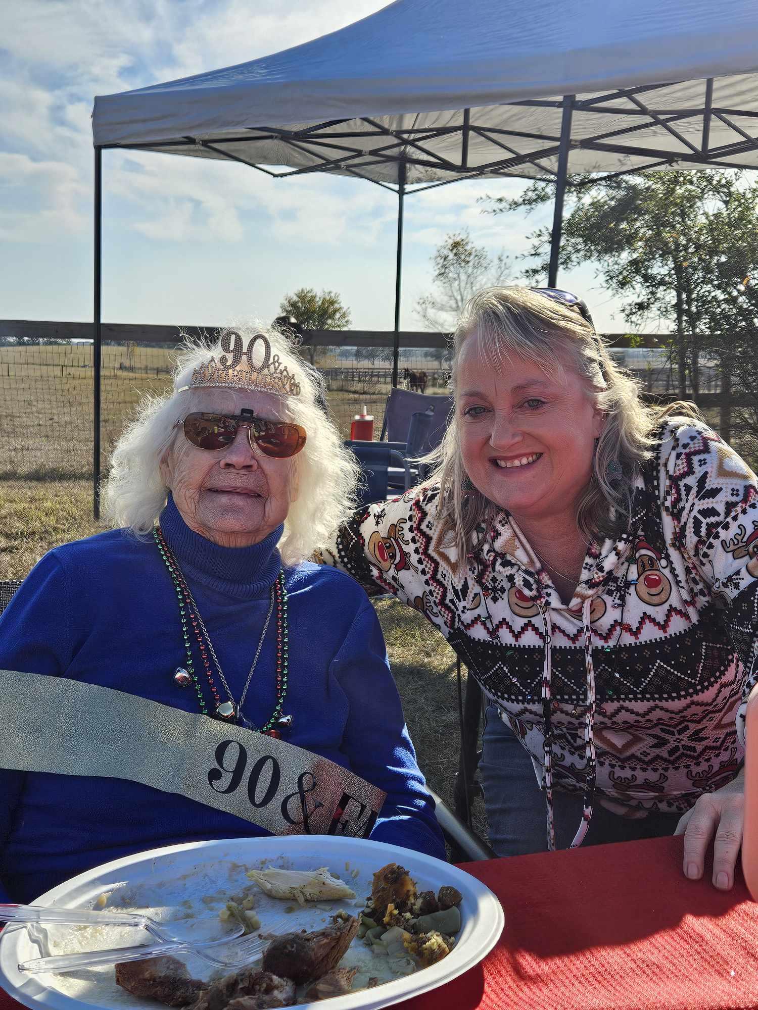 A joyful woman celebrates her 90th birthday outdoors, surrounded by family and decorations.