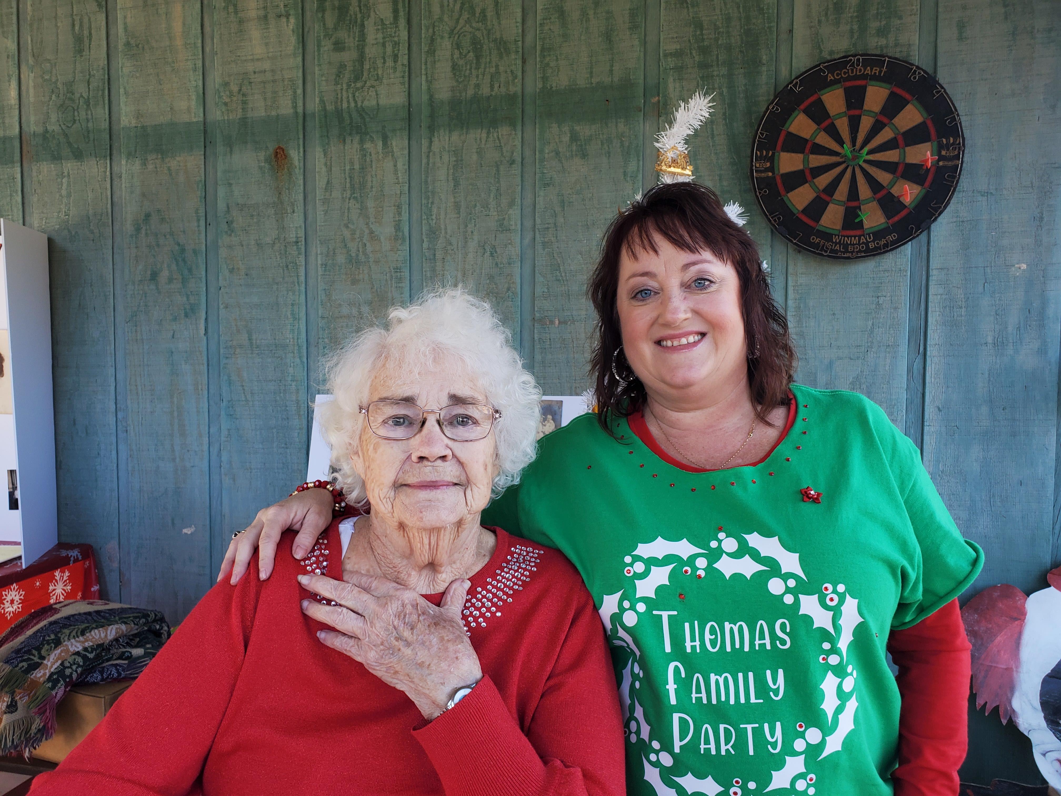 A cheerful gathering with two women, one elderly and one in green attire, smiling together outdoors.
