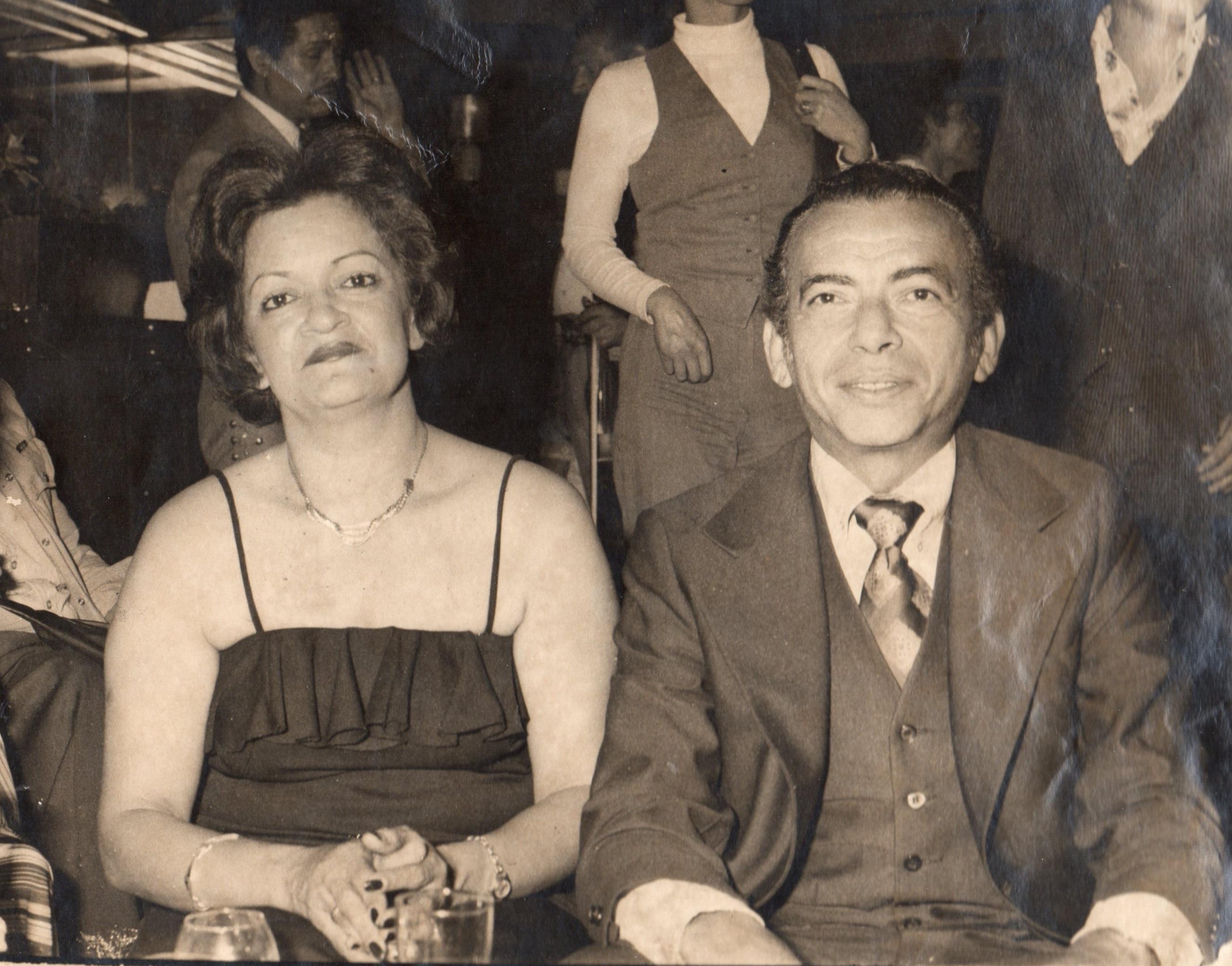 A couple sits closely together at a dimly lit venue, enjoying their time out in the 1970s.