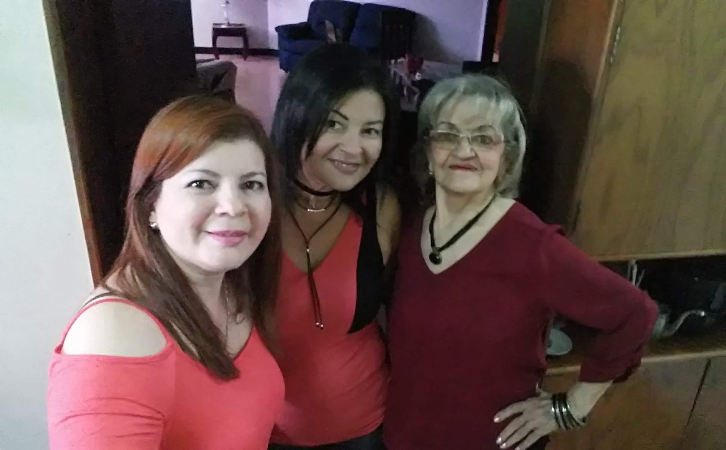 Three women pose joyfully while wearing red outfits in a warm living room.