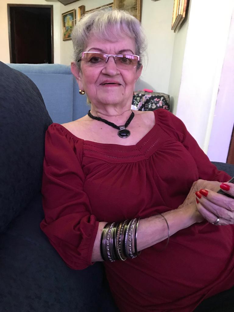 Senior woman with glasses sits comfortably, dressed in a red outfit, holding a phone and smiling.