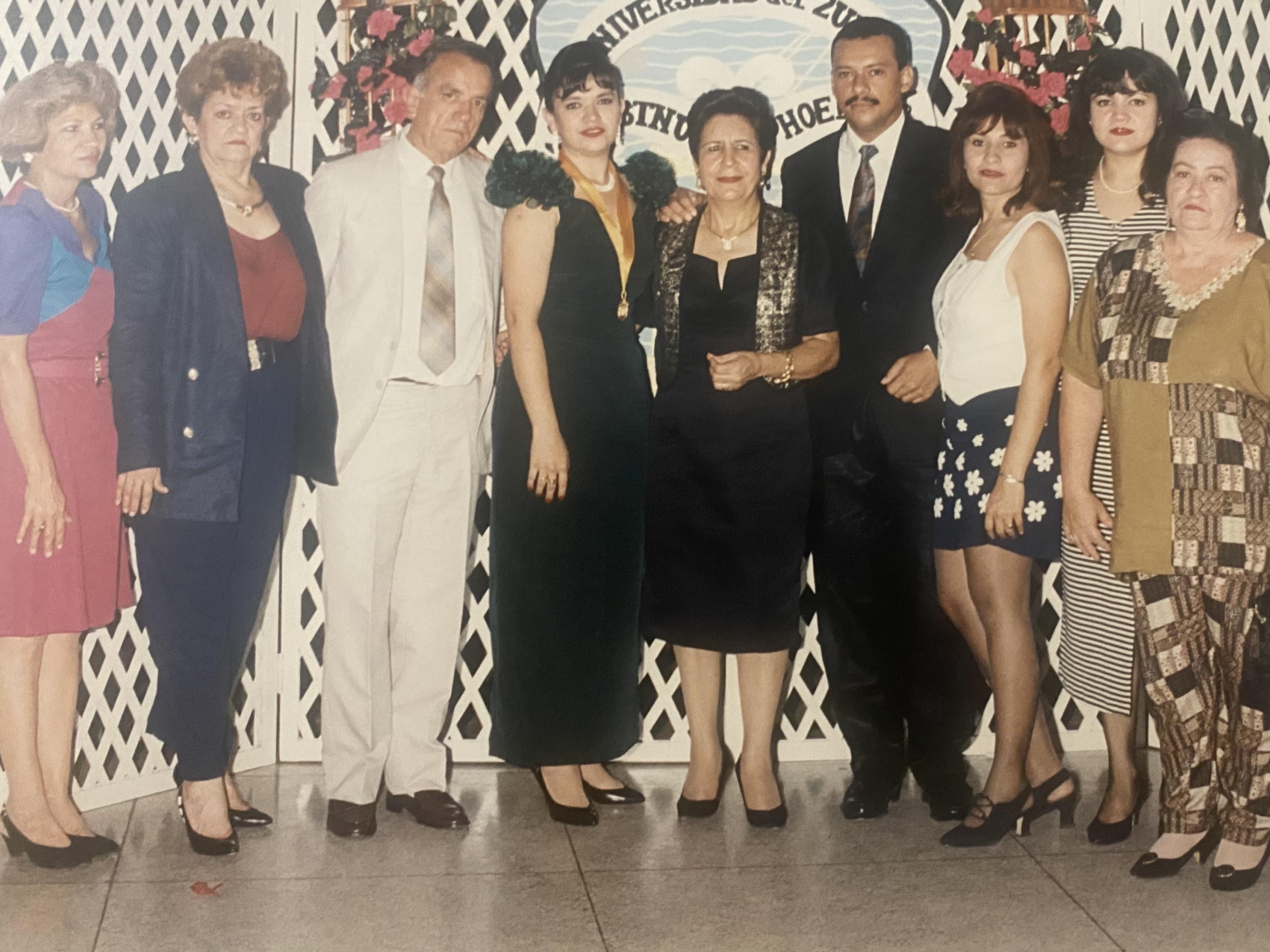 A group of well-dressed individuals stand together in a decorated hall, enjoying a special occasion.