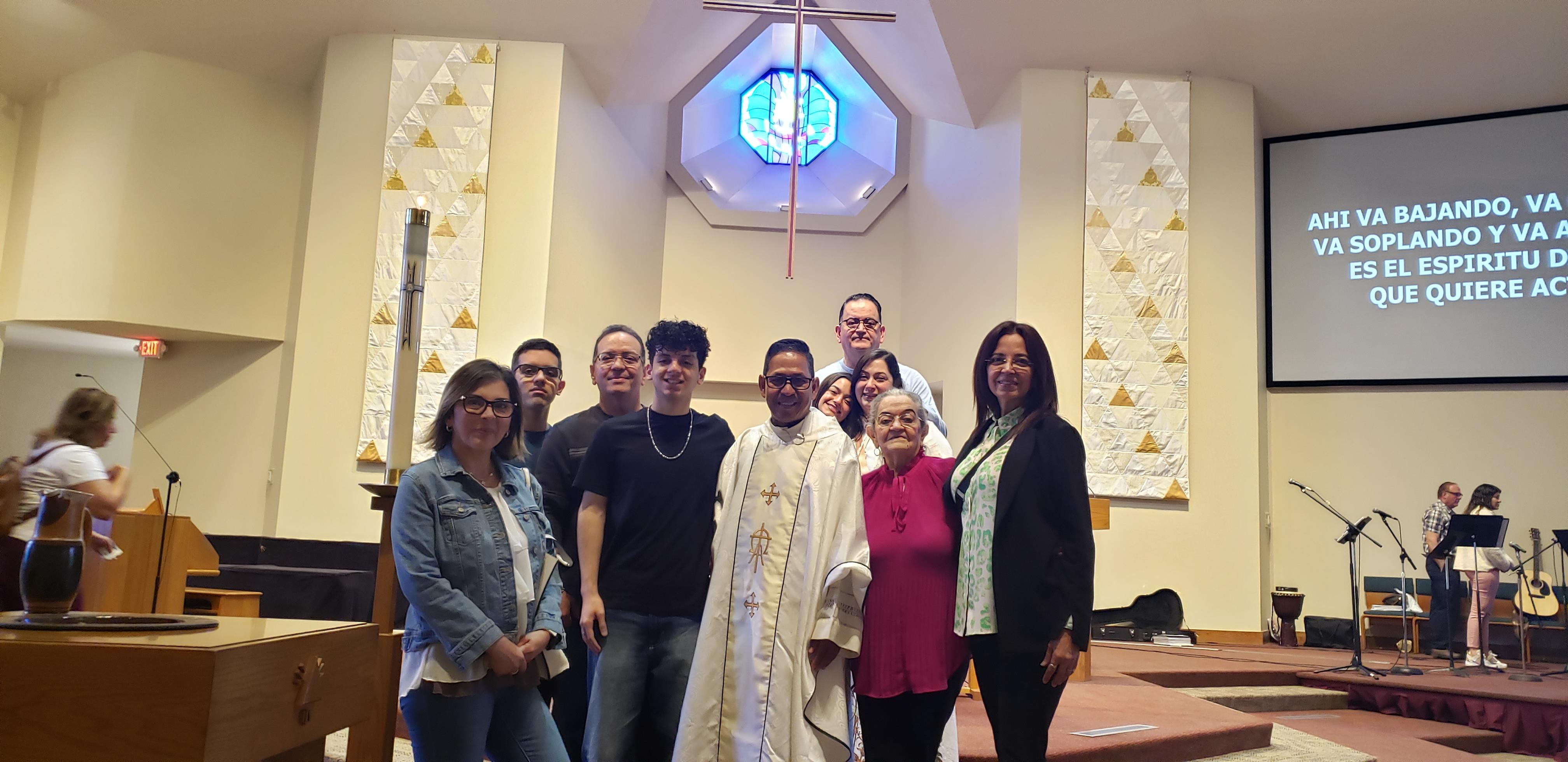 People gather for a special ceremony in a church with a priest, smiling and celebrating together.