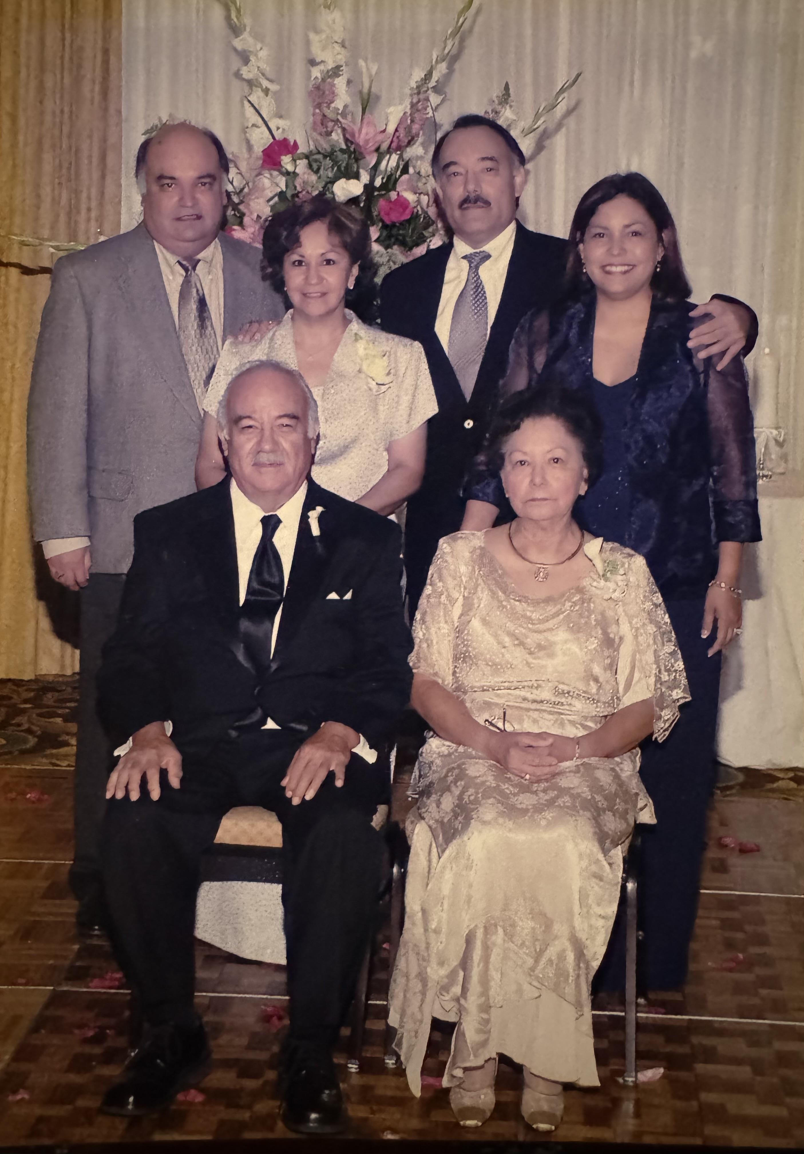 A group of six relatives poses together, showcasing their formal outfits in a festive setting.
