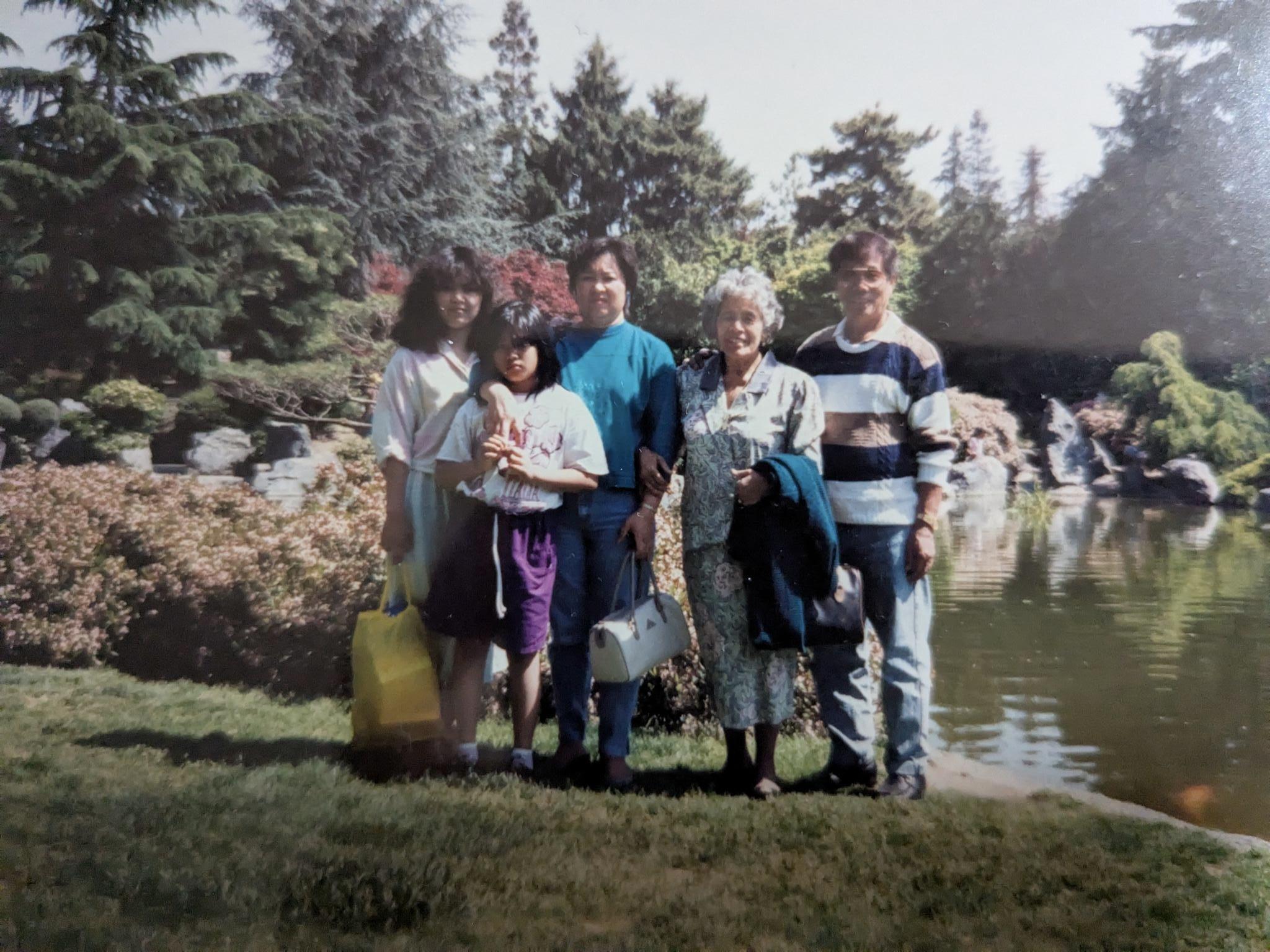 Group of five people standing together by a pond, enjoying a sunny day outdoors.