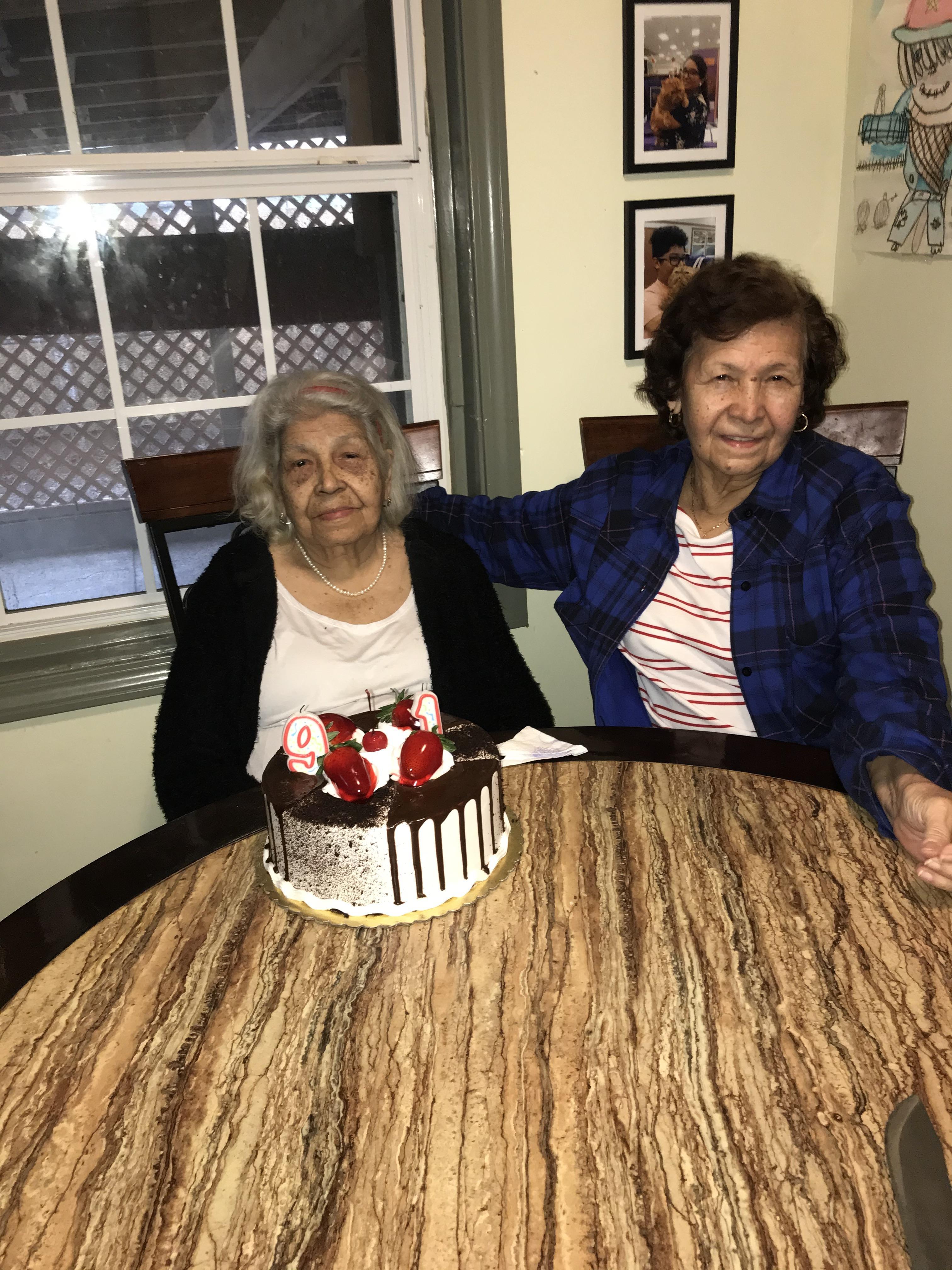 Two women enjoy a special moment together at a dining table with a cake.