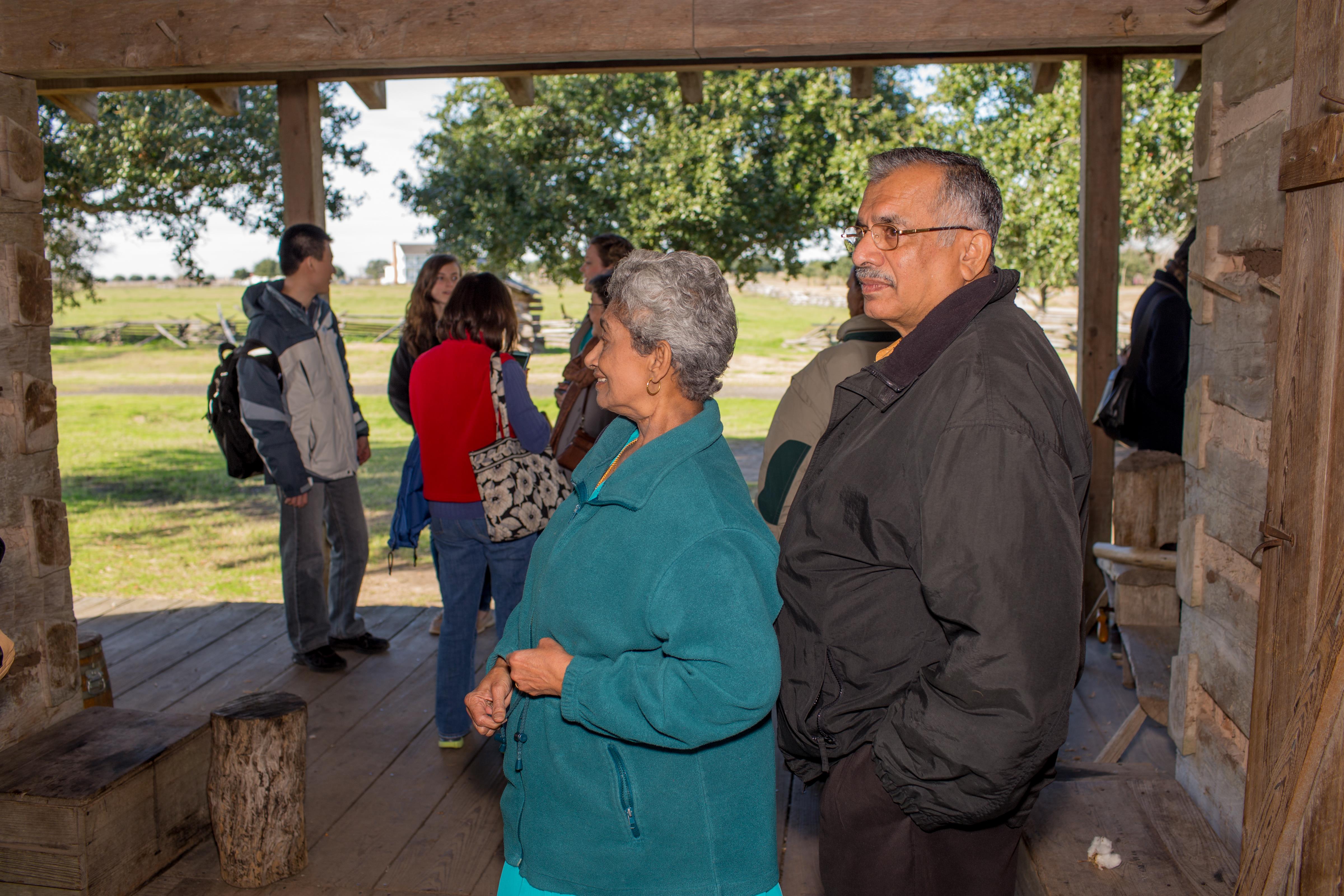 Numerous individuals mingle and converse in a cozy outdoor setting under a shelter.