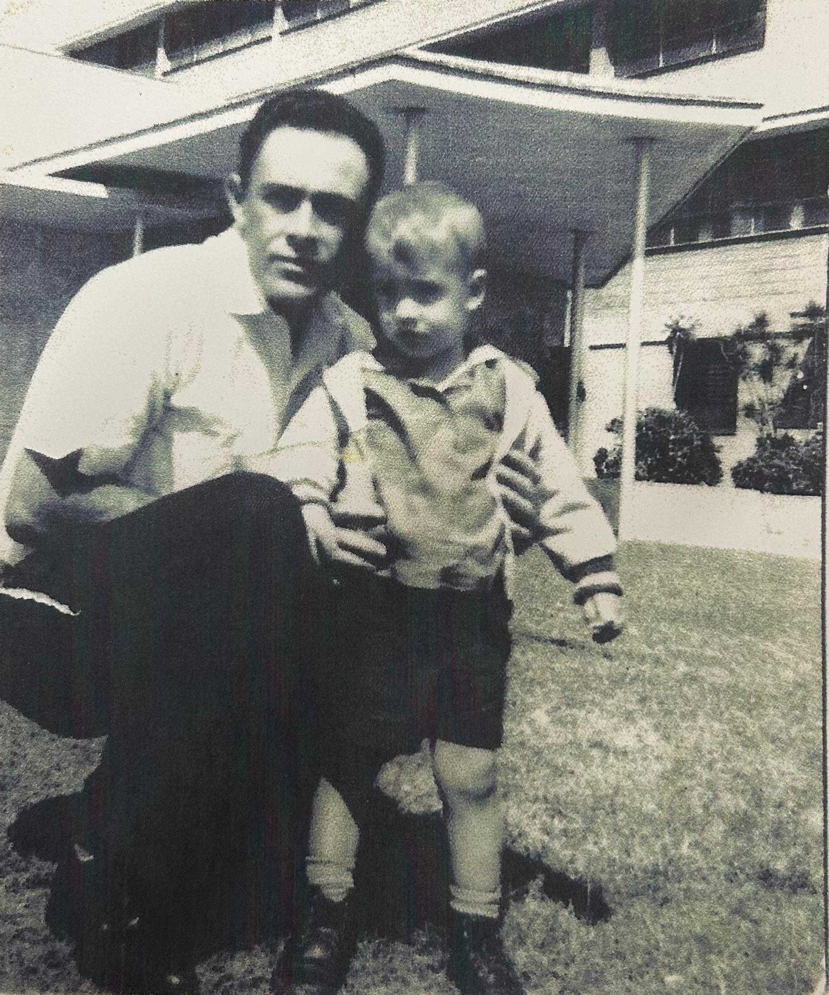 A father kneels next to his young son in a grassy backyard filled with sunshine and laughter.