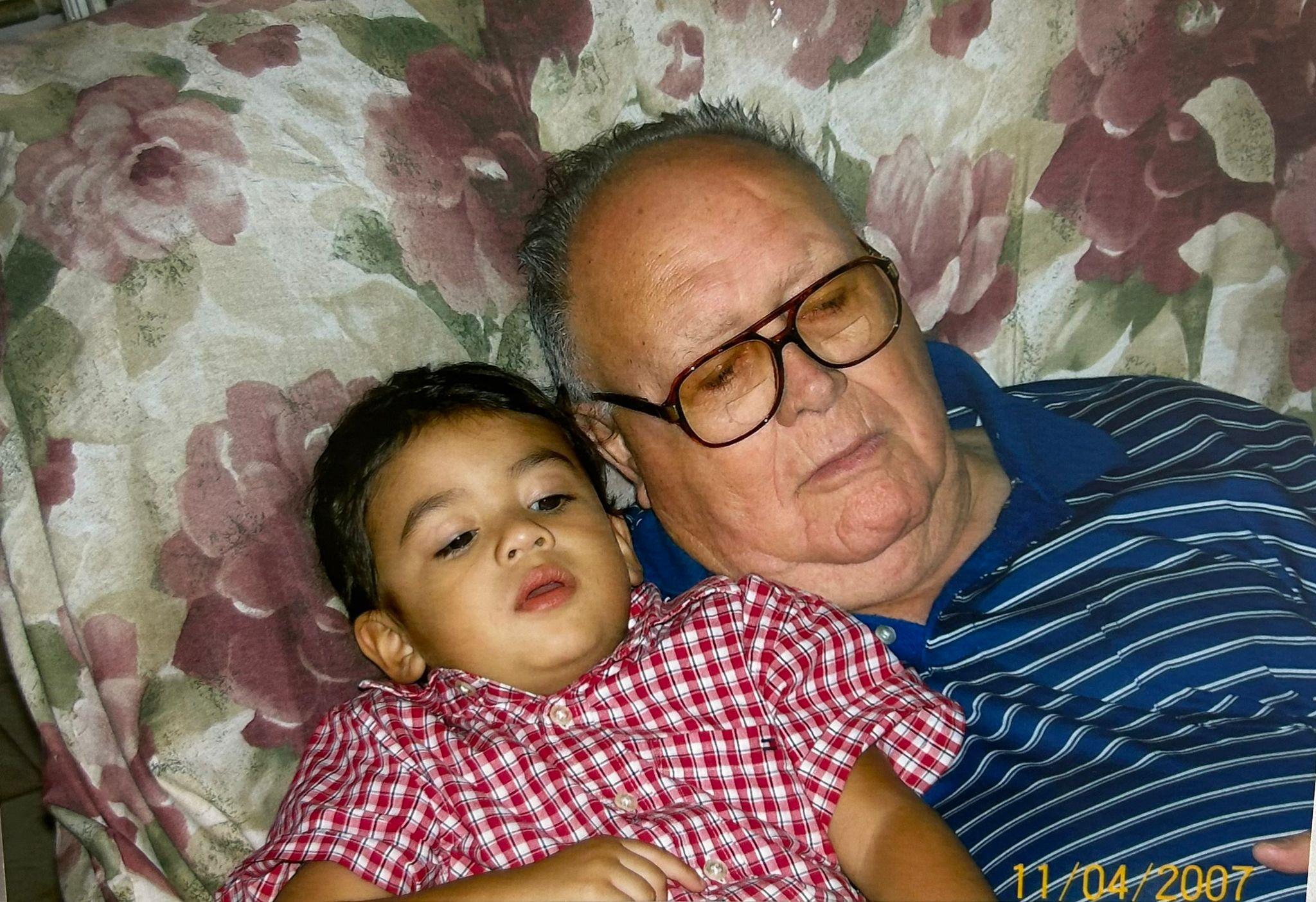 A grandfather and his grandson are resting together on a comfortable floral couch, enjoying time.