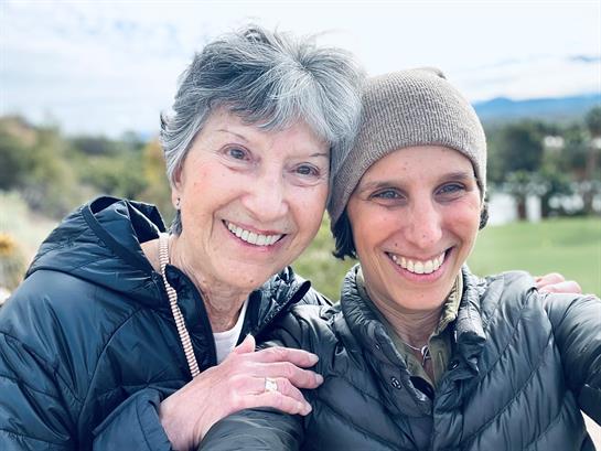 Two women smile brightly for a close-up selfie, showcasing their happiness and connection in nature.