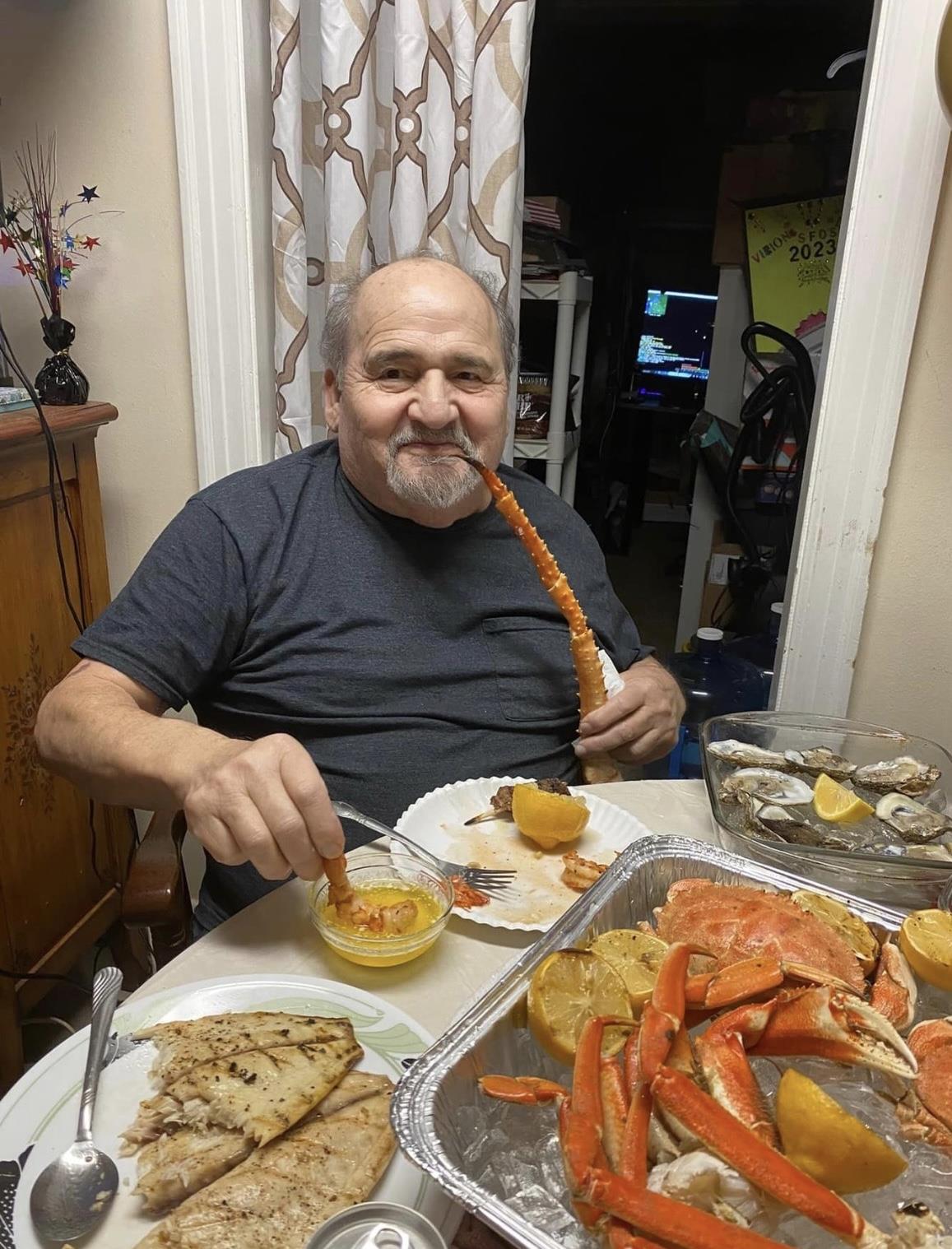 Man smiles while eating crab and dipping it in sauce during a home celebration.