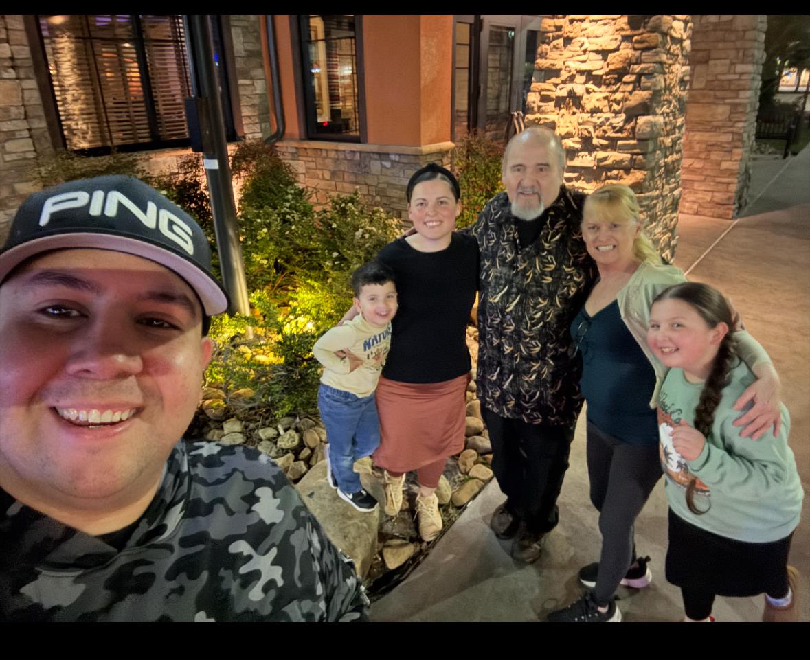 Group of six people smile together in a charming outdoor area at night.
