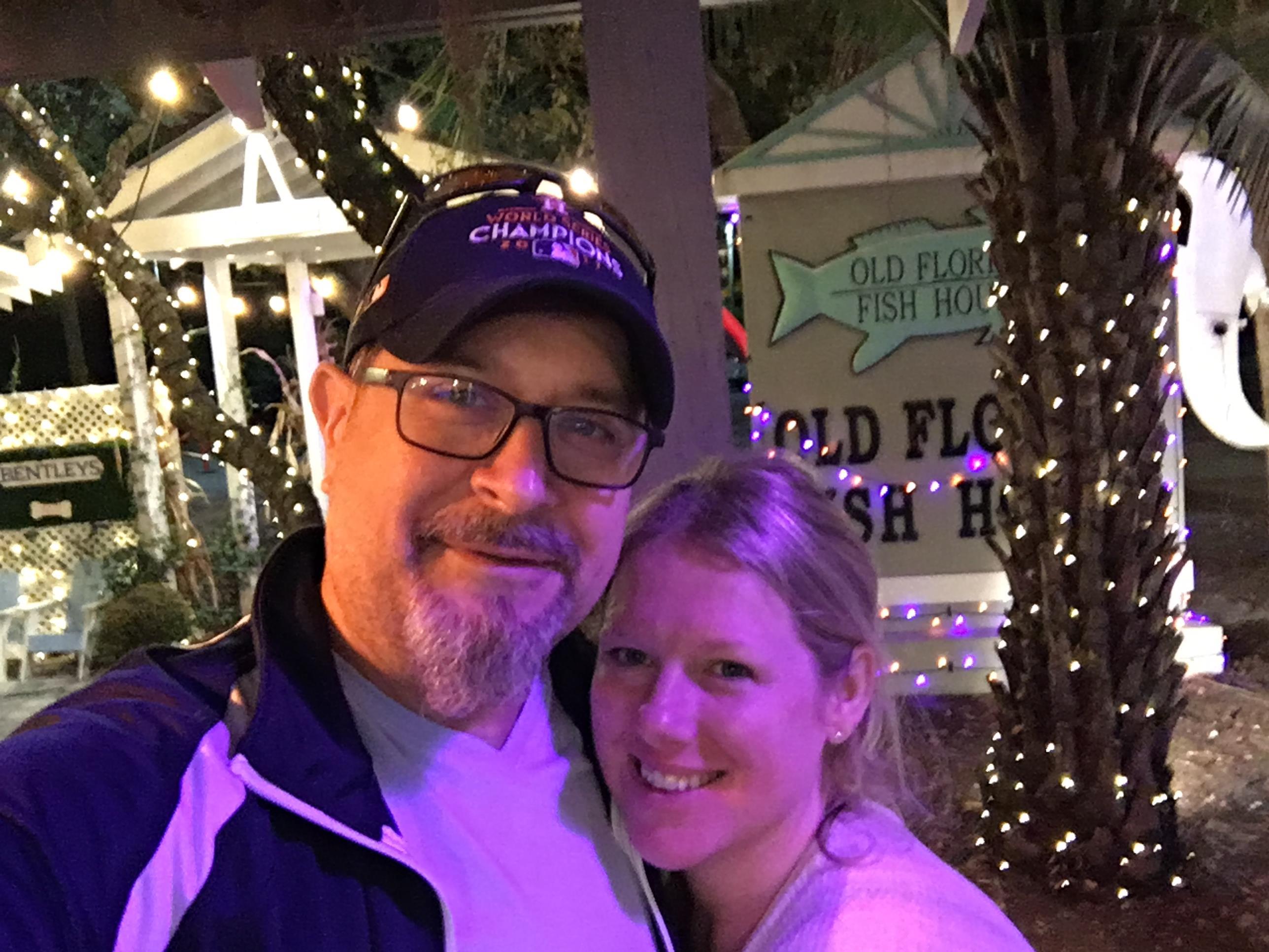 A couple stands close together under colorful lights, smiling and enjoying a fun night out.