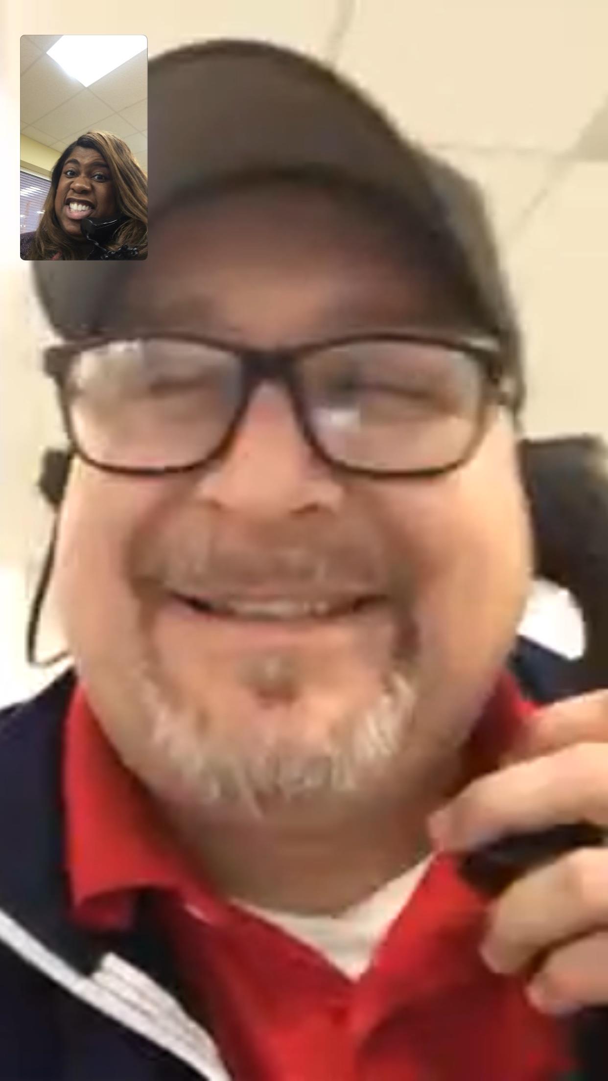 Man with glasses smiles while speaking on the phone in a relaxed indoor environment.