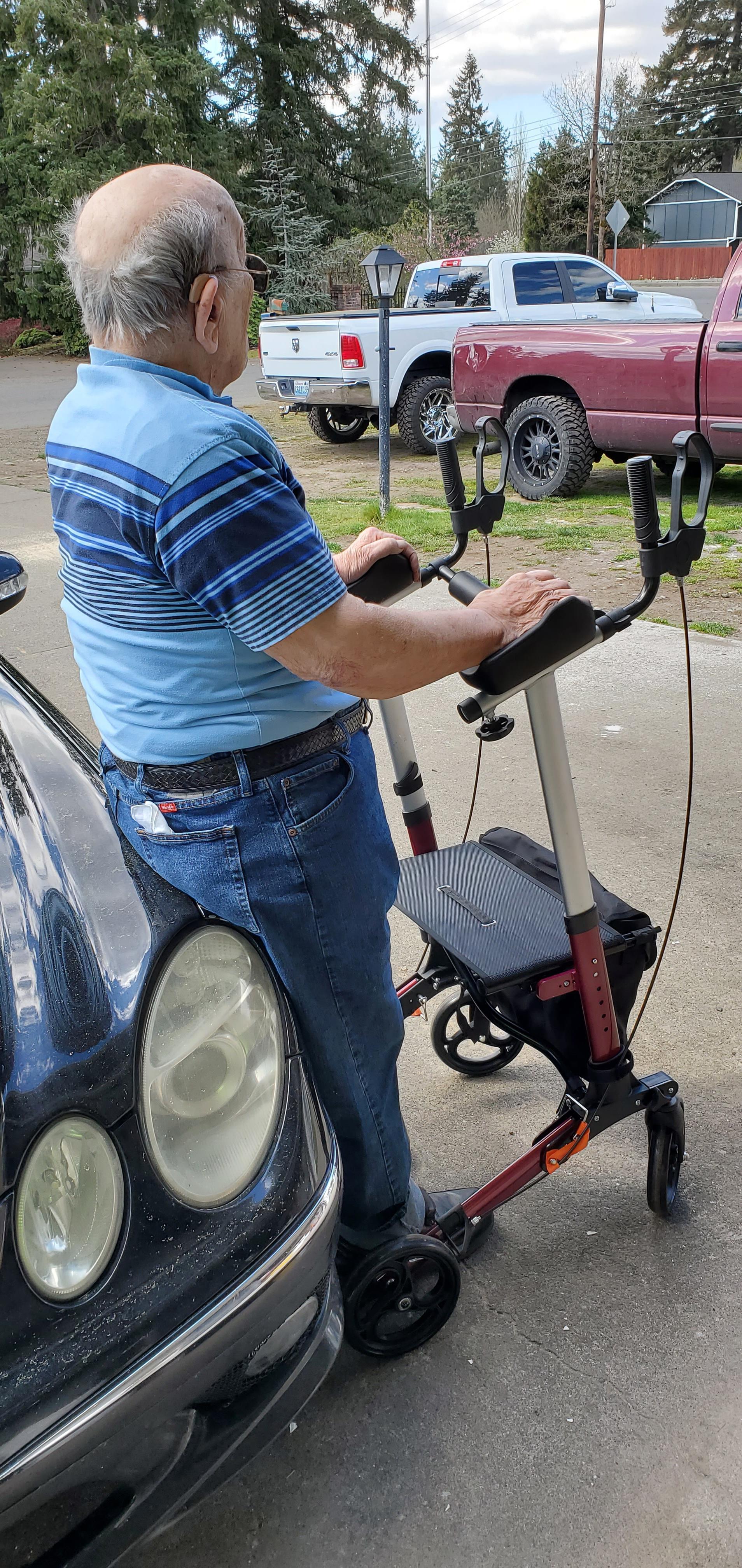 Man rides a mobility scooter beside a parked car on a sunny day, enjoying his time outside.