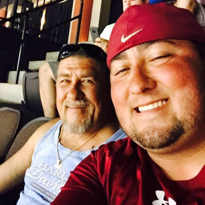 Two men are smiling broadly, enjoying a sports game together in the stadium seats.