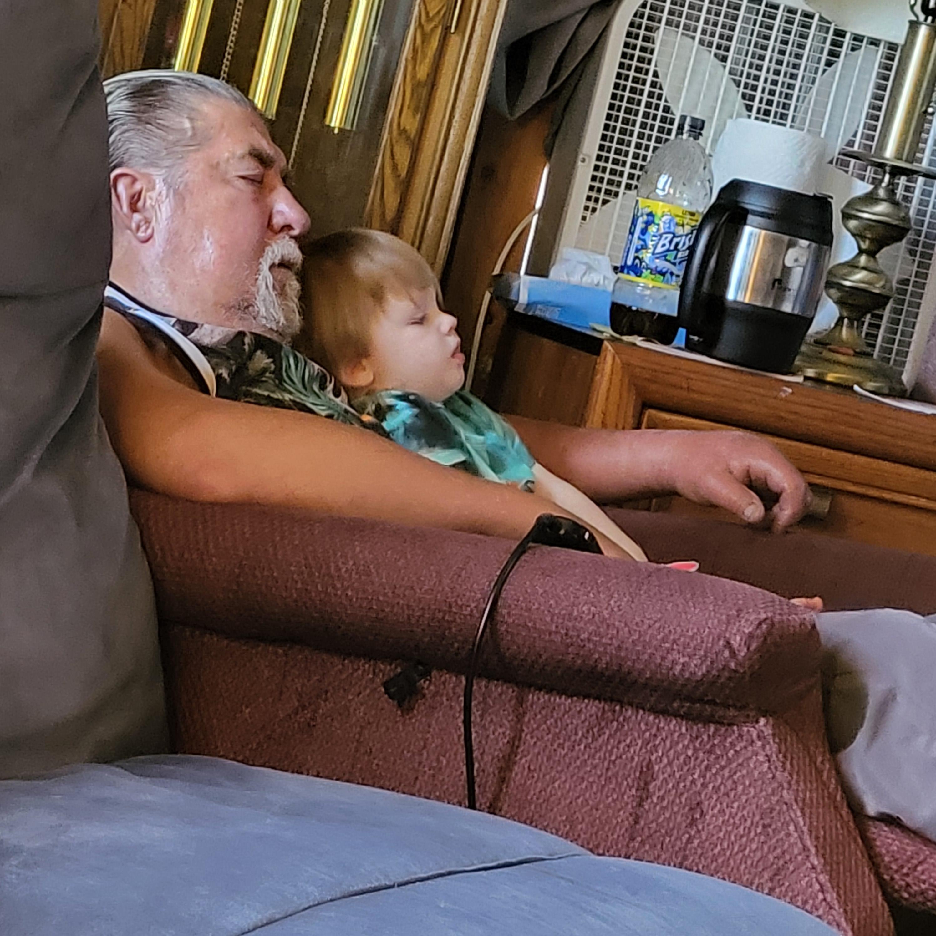 An elderly man and a child relax together on a comfy chair, savoring each other's company.