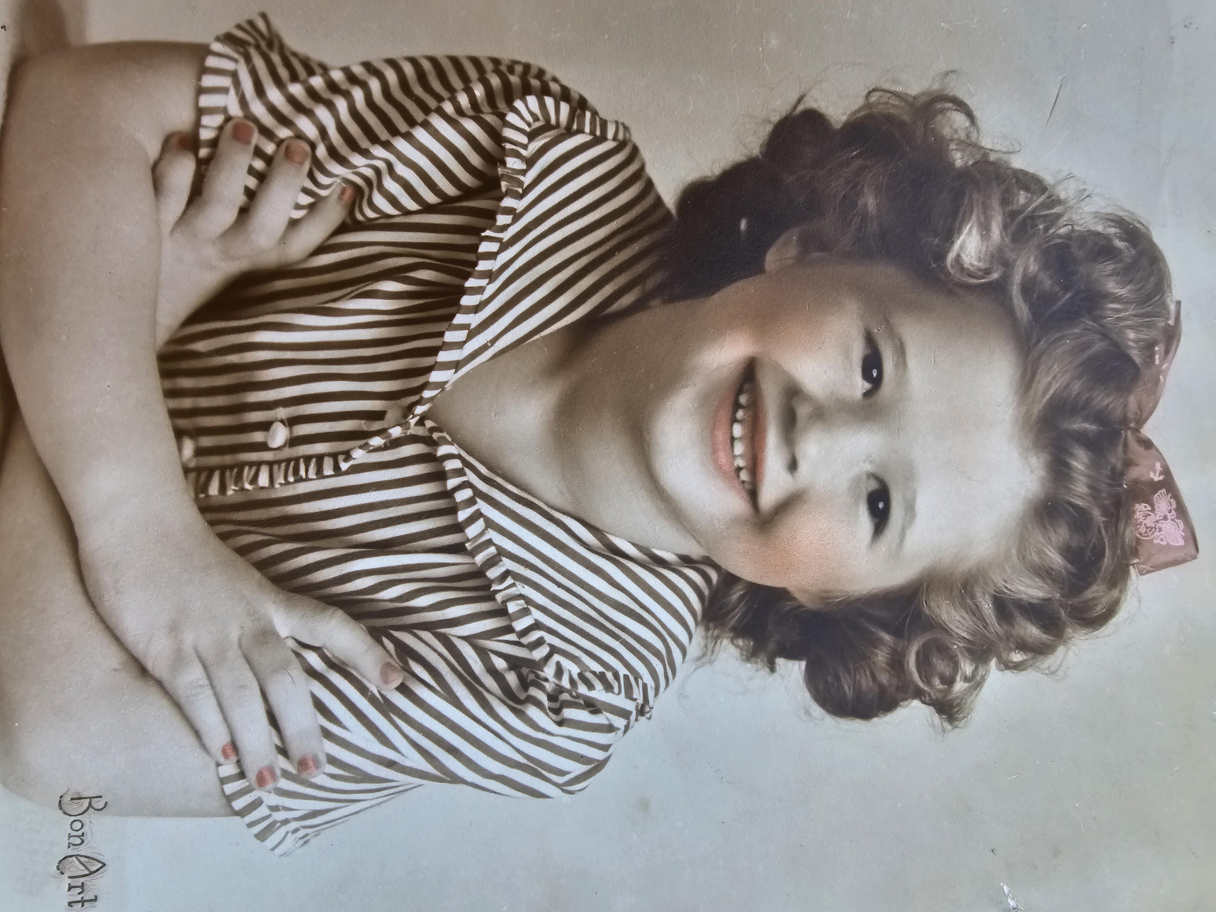 A curly-haired child smiles indoors in a striped shirt, enjoying a joyful moment.