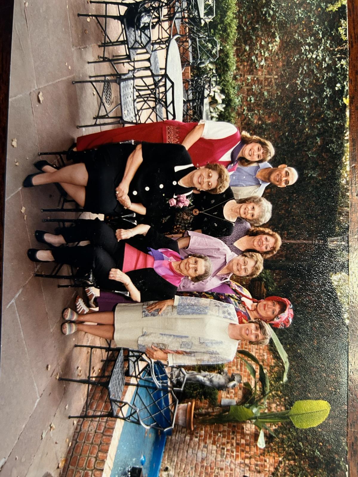 A cheerful group of friends smiles together in a sunny garden filled with greenery.