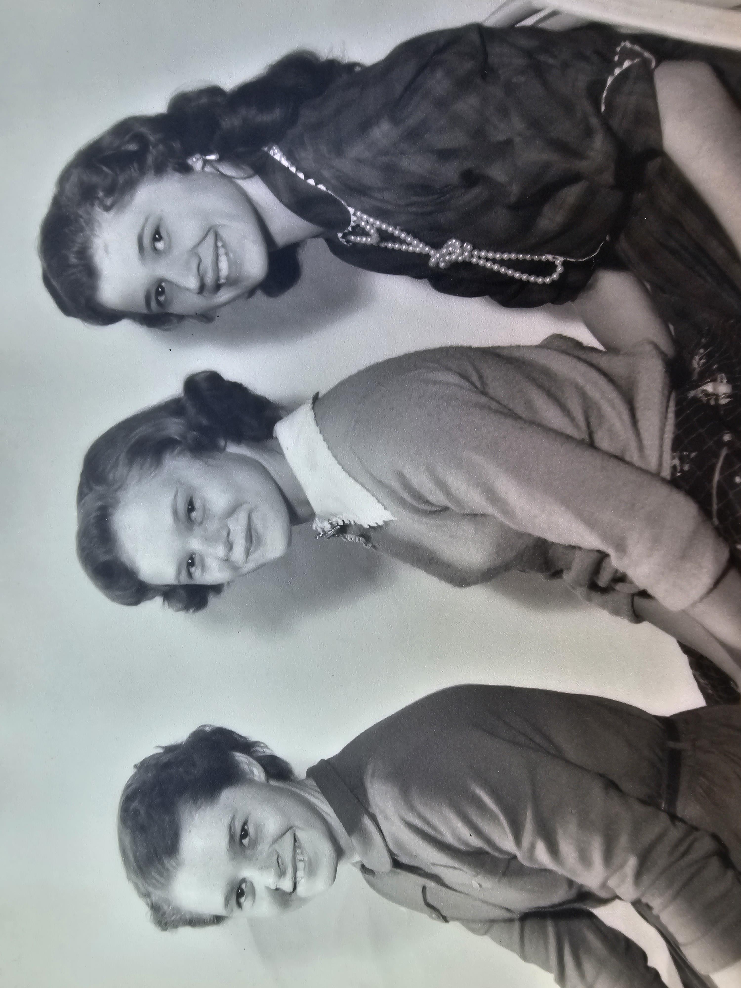 Three women are smiling together, dressed in stylish, vintage clothing from the 1950s.