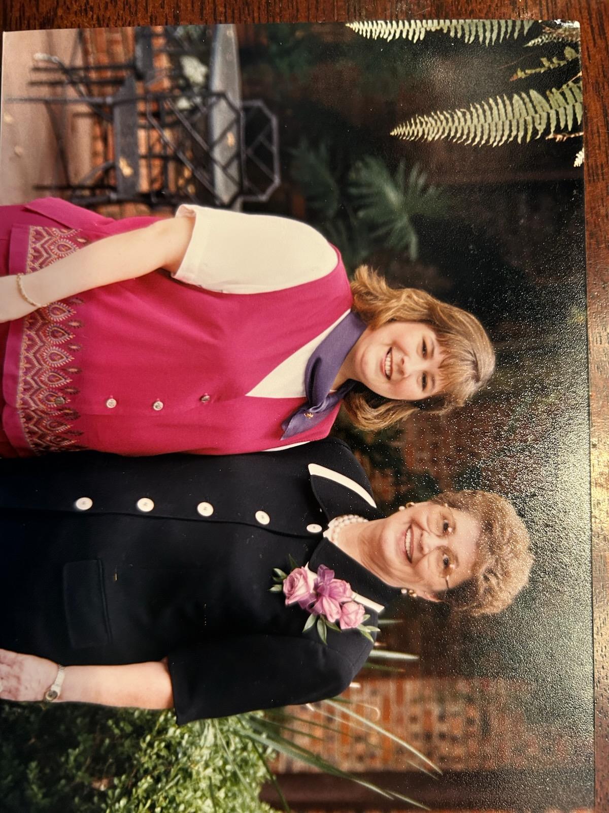 Two cheerful women stand side by side in a beautiful garden, enjoying a joyful moment.
