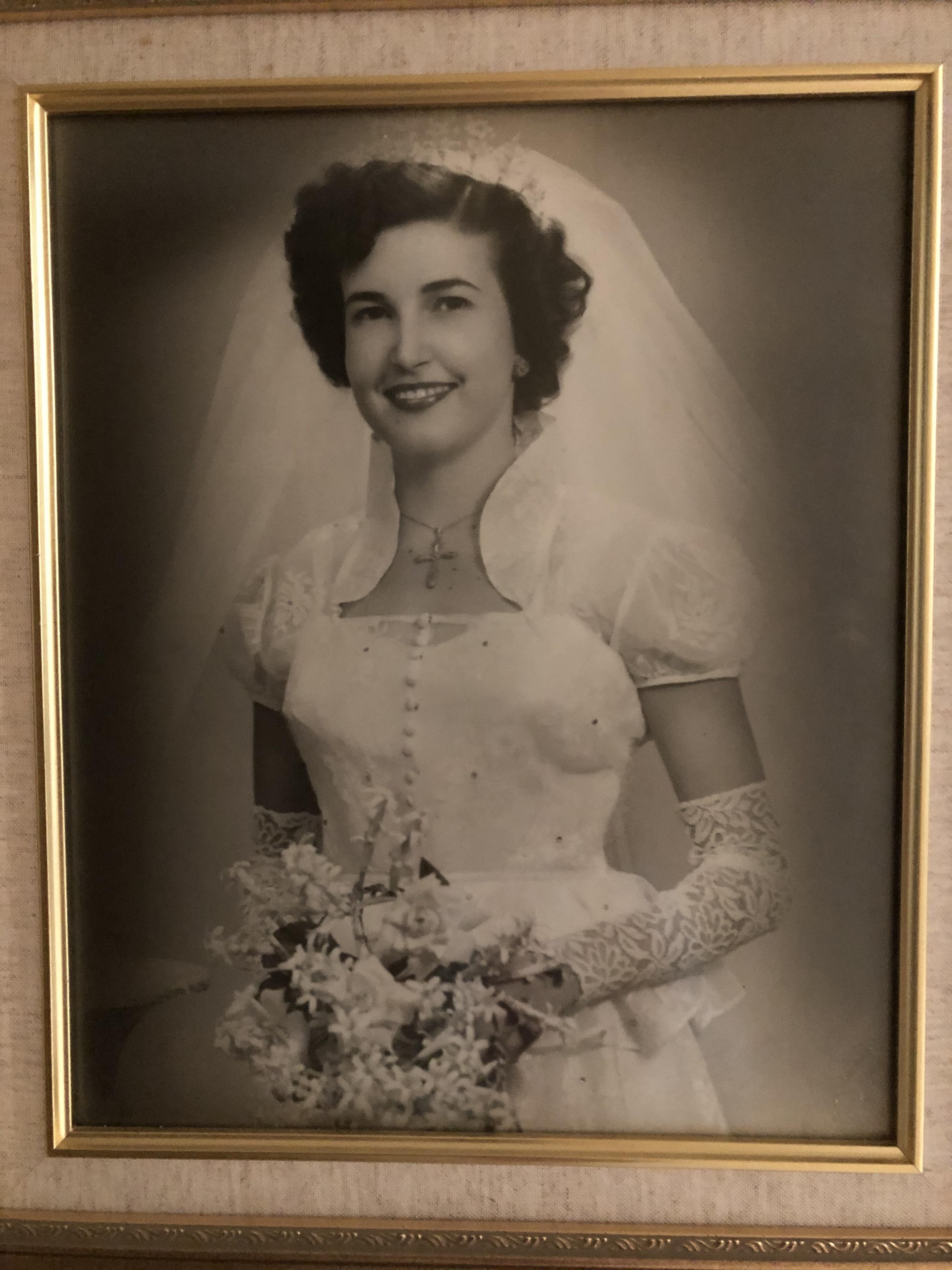 A bride smiles while holding a bouquet, dressed in a vintage wedding gown with lace details.