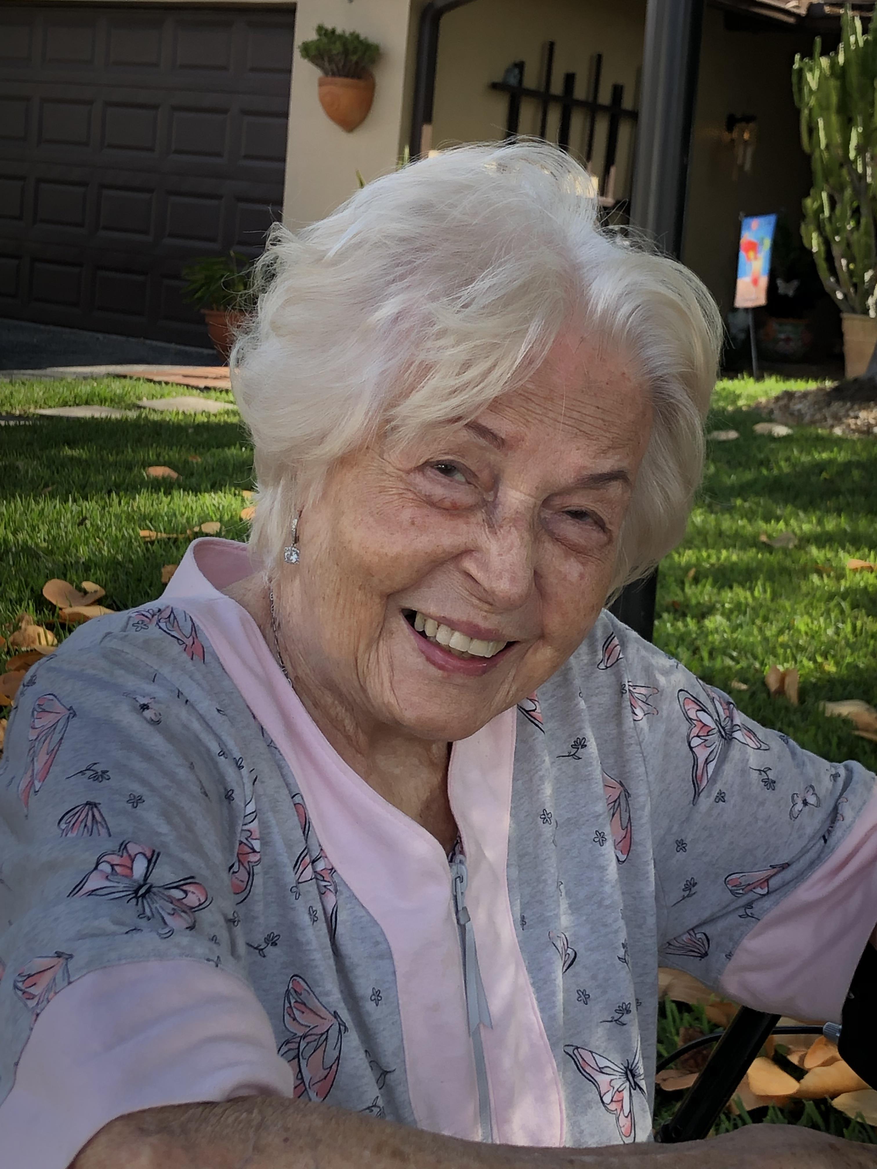 An elderly woman enjoys a sunny afternoon in her garden, smiling warmly and radiating joy.